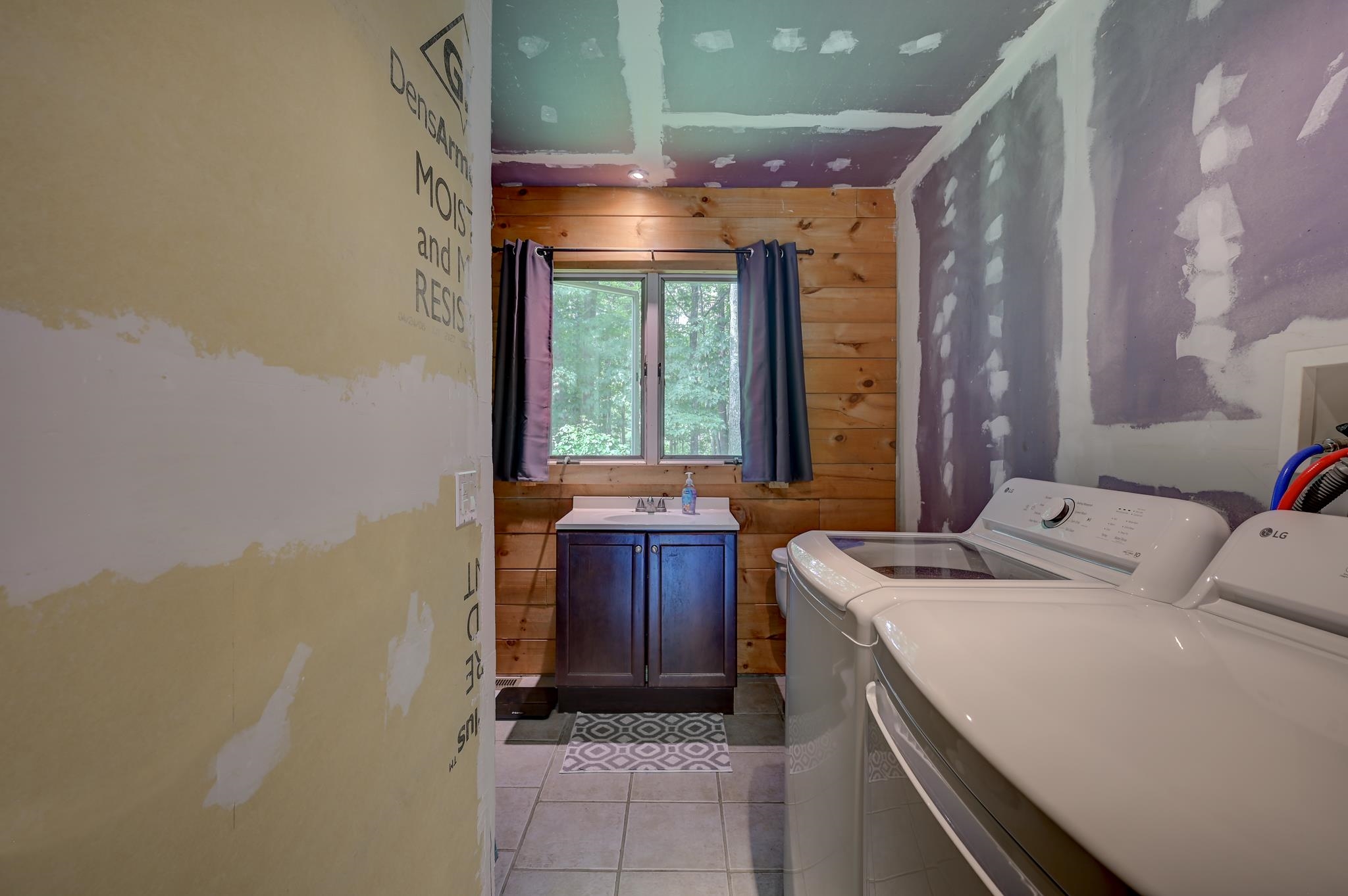 Laundry room with washer and dryer, a blue sink vanity, wood walls, and unfinished drywall.
