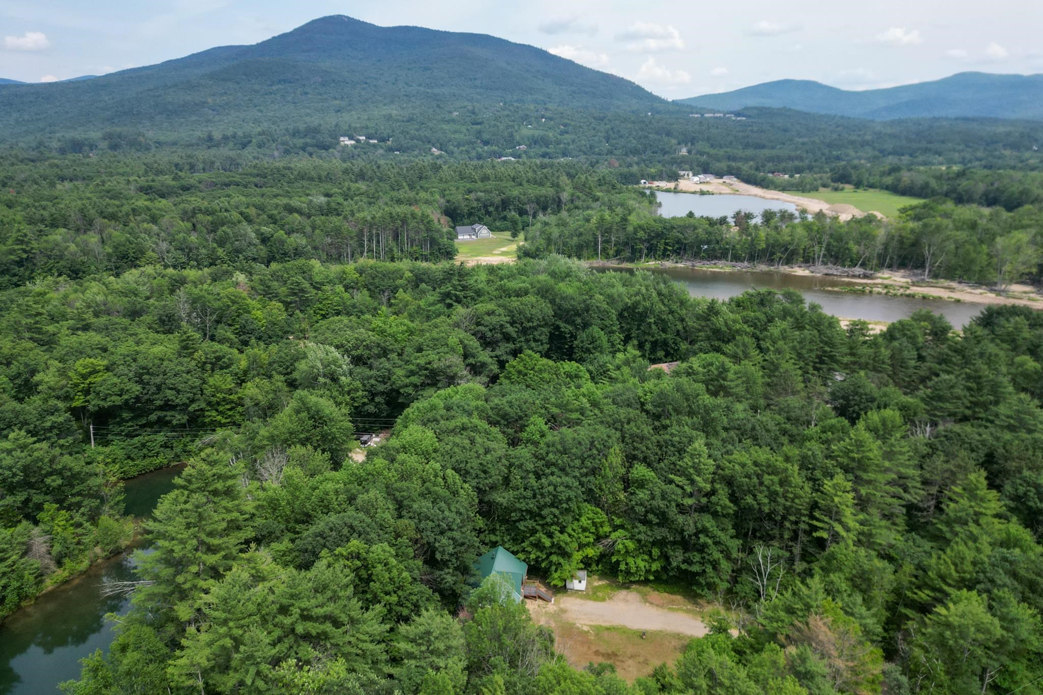 Aerial view of a green-roofed building in dense forest, with winding water and mountains beyond.