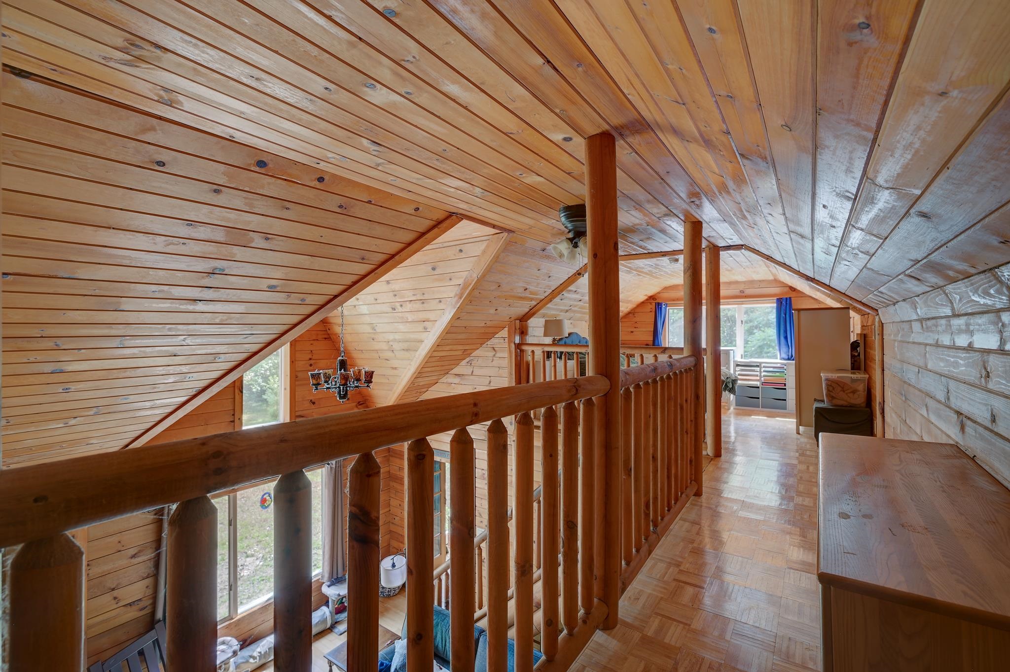 Wood-paneled loft hallway with a vaulted ceiling, log railing, and parquet floor.
