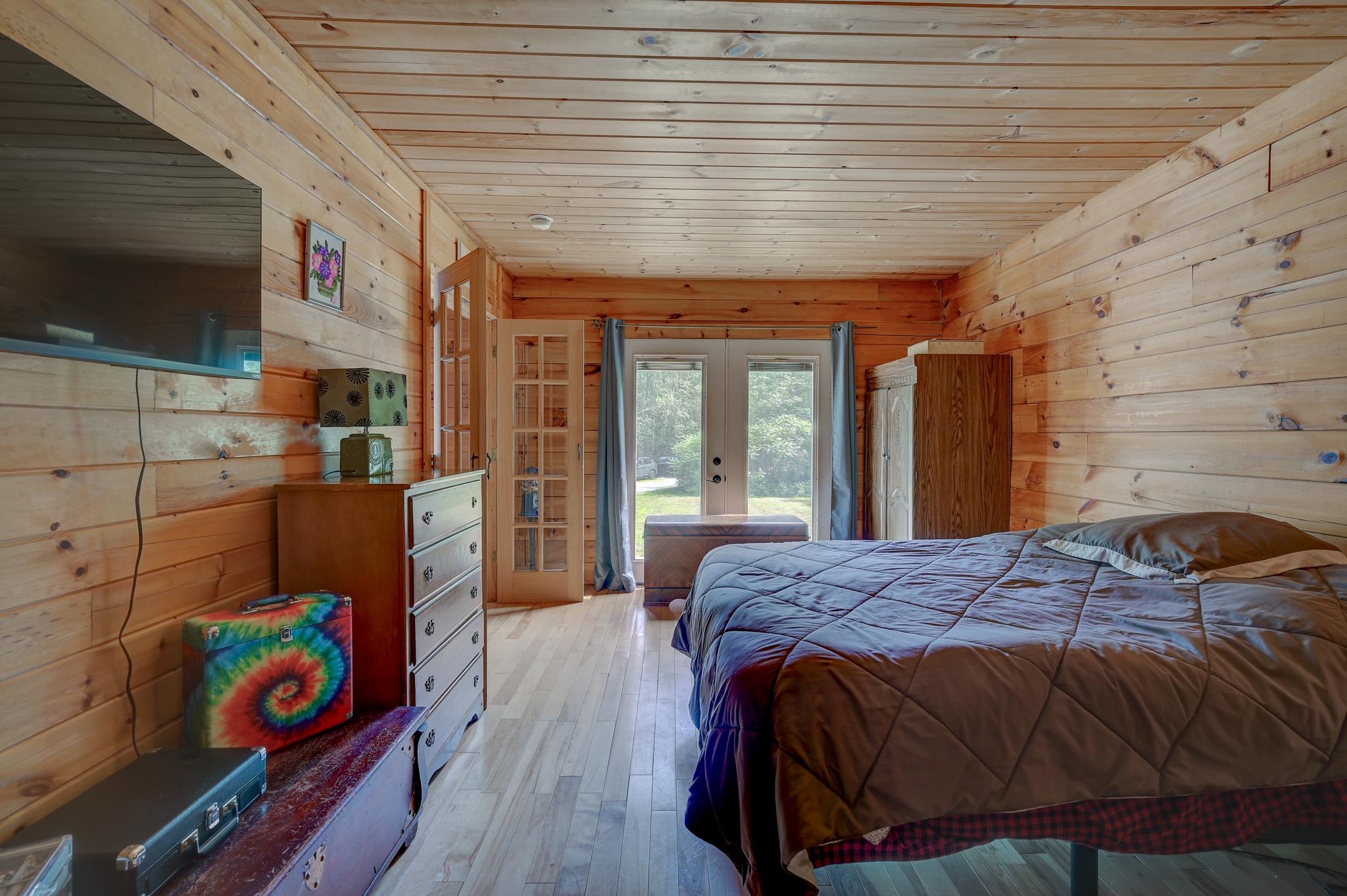 Wood-paneled bedroom with a large bed and glass doors opening to greenery.