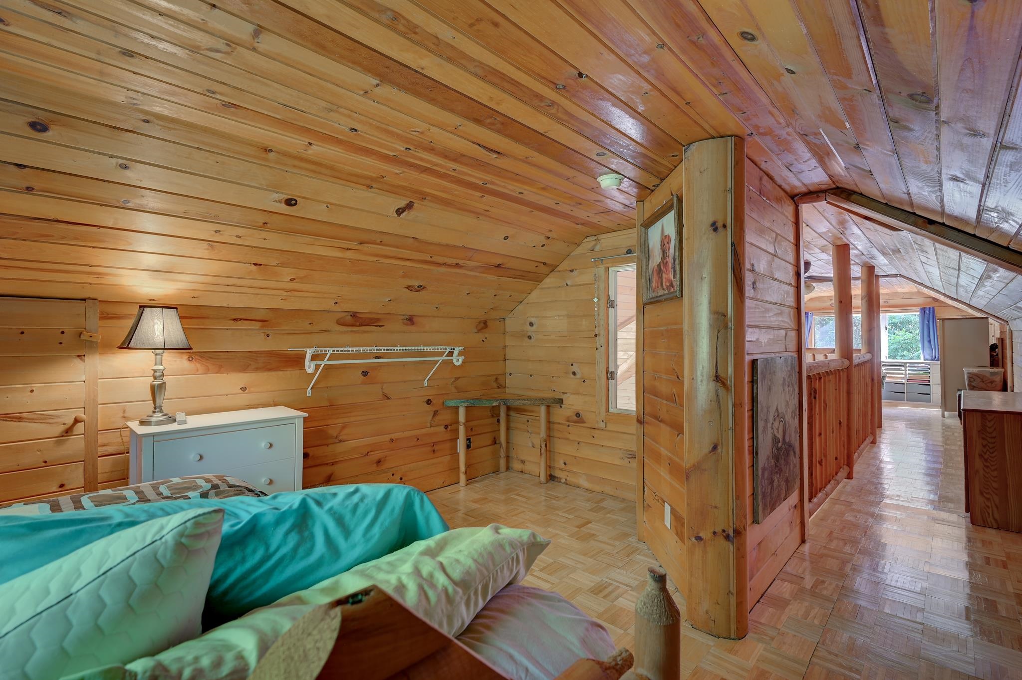 Loft bedroom with turquoise bedding, knotty-pine walls, and a wood-paneled hallway.