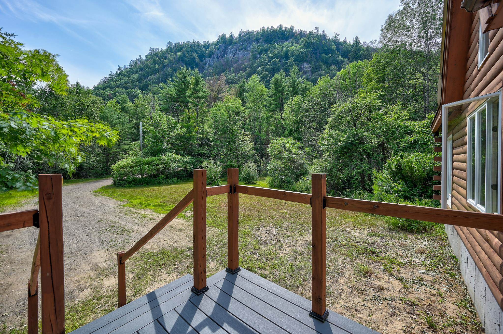 Wooden deck overlooking a grassy yard, gravel driveway, and wooded mountain ridge.