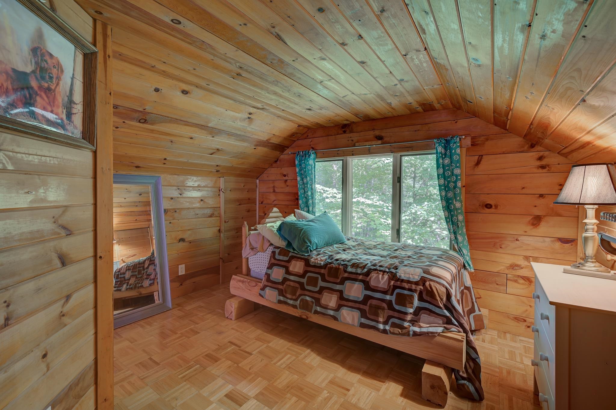 Wood-paneled bedroom with a patterned bed beneath a wide window and teal curtains.