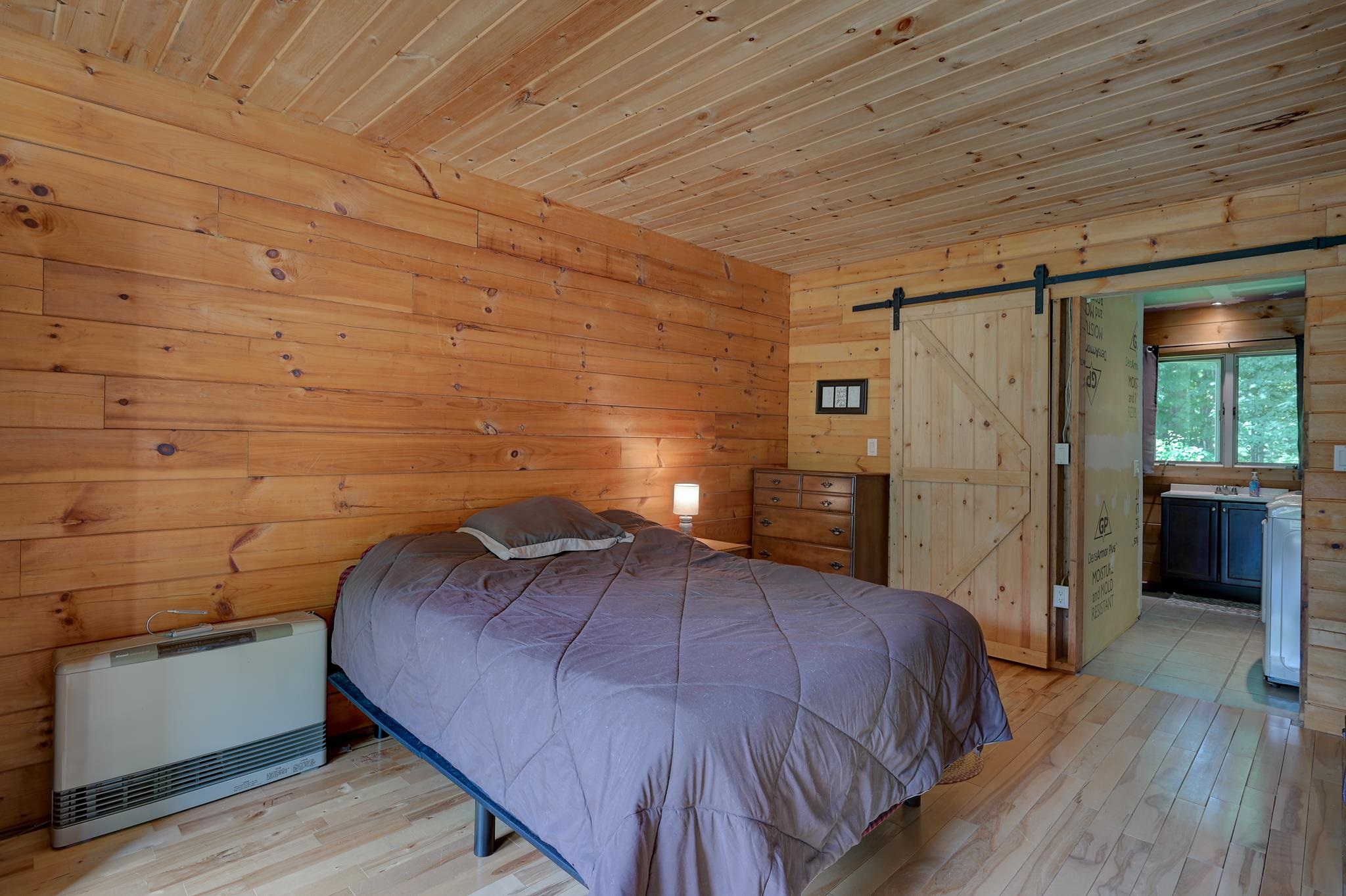 Bedroom with knotty pine walls, a gray-covered bed, and a sliding barn door to the bathroom.