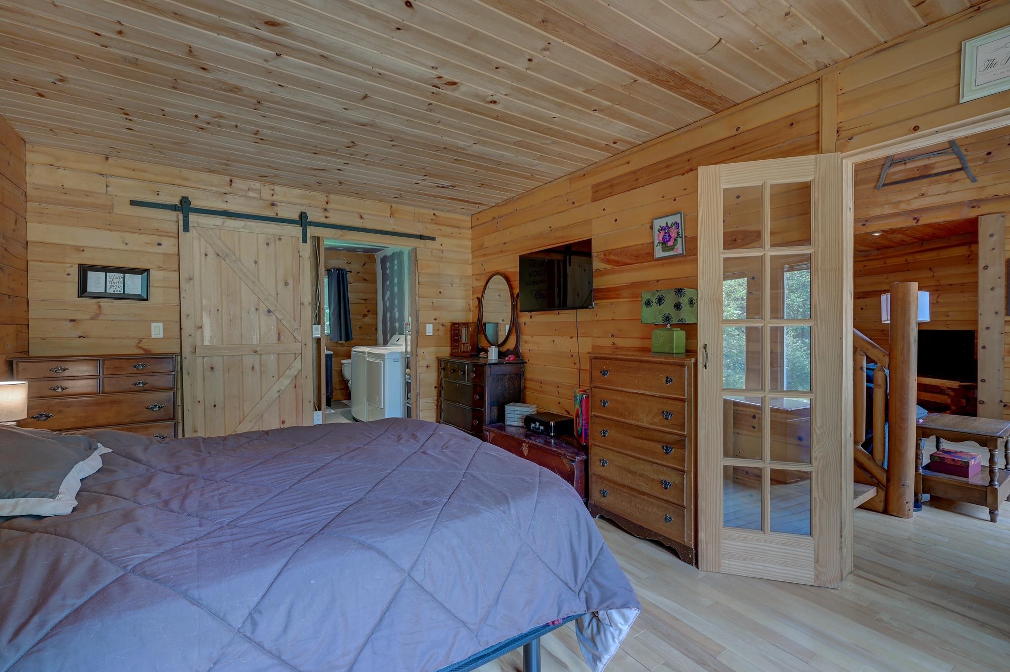 Wood-paneled bedroom with a large bed, sliding barn door, and glass-paneled doorway to a staircase.