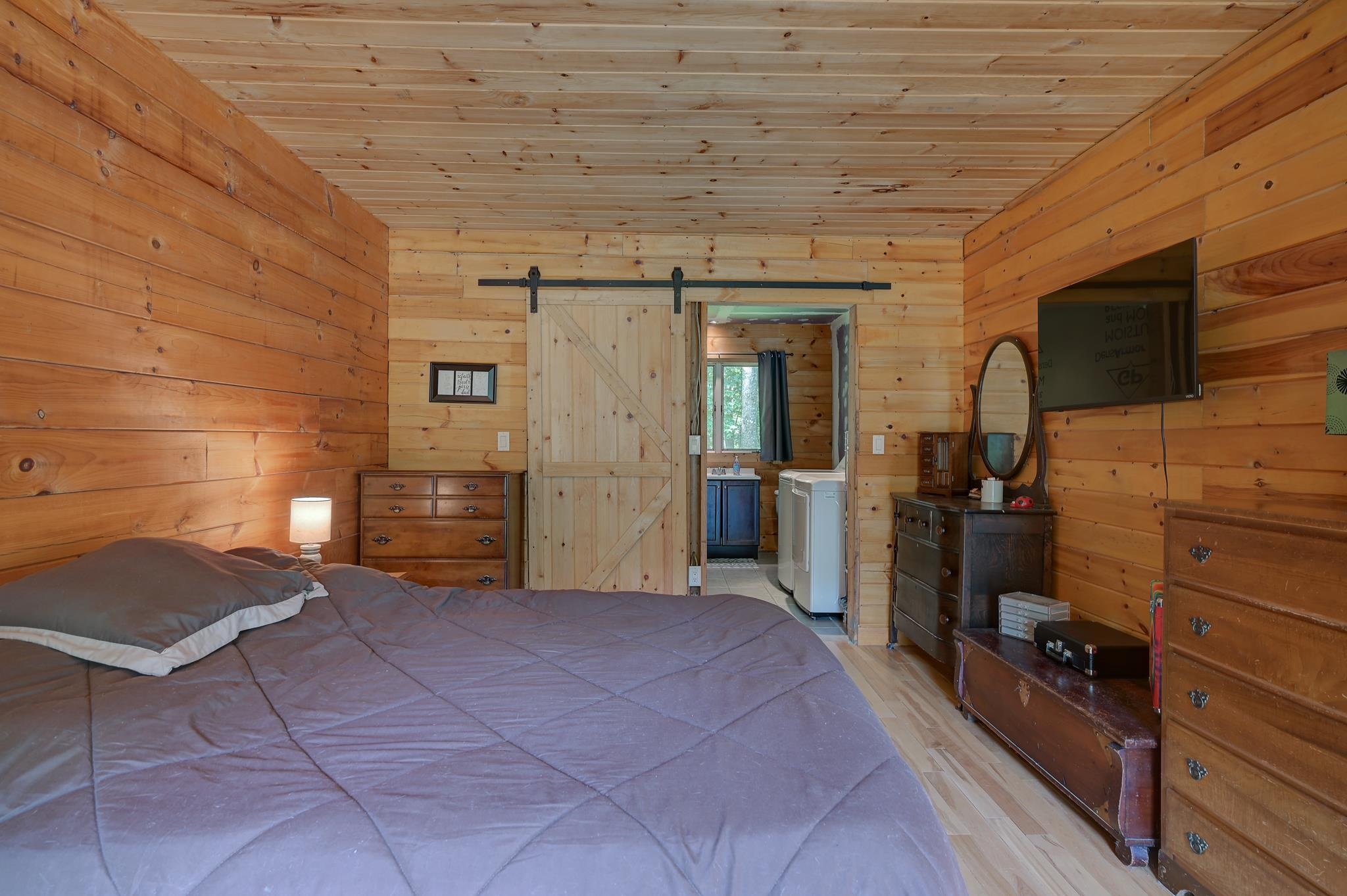 Furnished bedroom with knotty-pine walls, a large bed, and a sliding barn door.