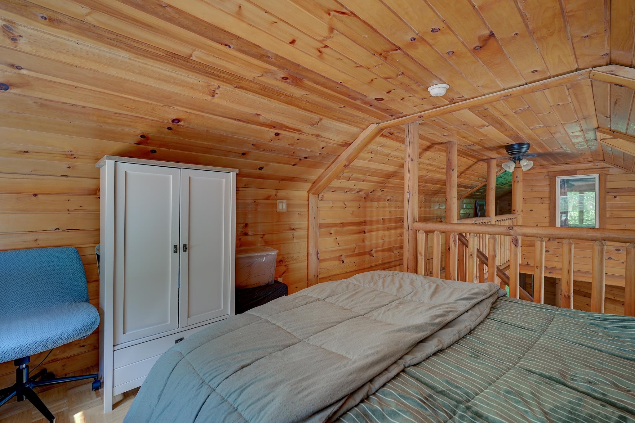 Loft bedroom with a bed beneath a sloped pine ceiling and a timber railing.