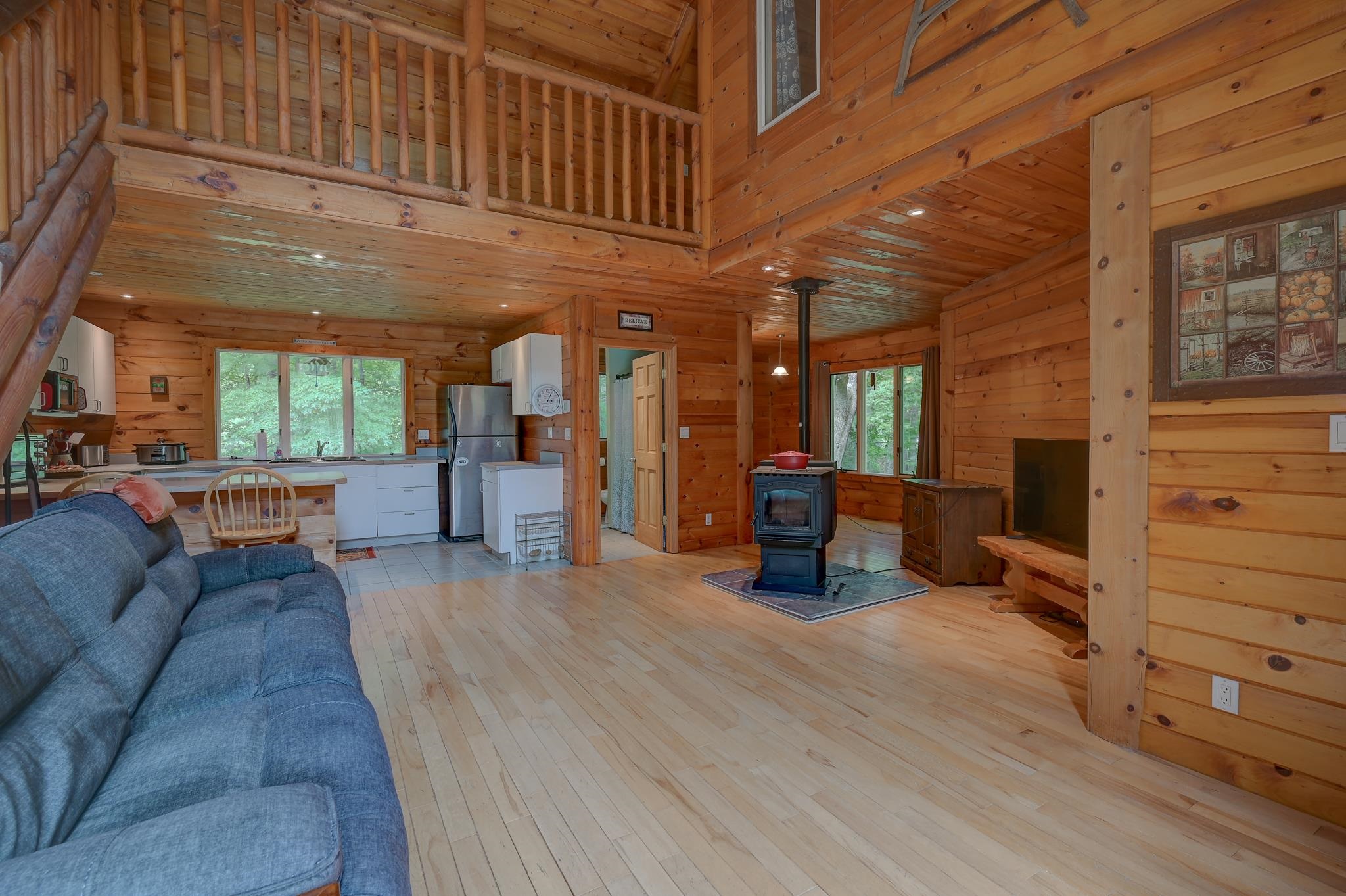 Cabin great room with a loft balcony, open kitchen, blue sofa, and black wood stove.