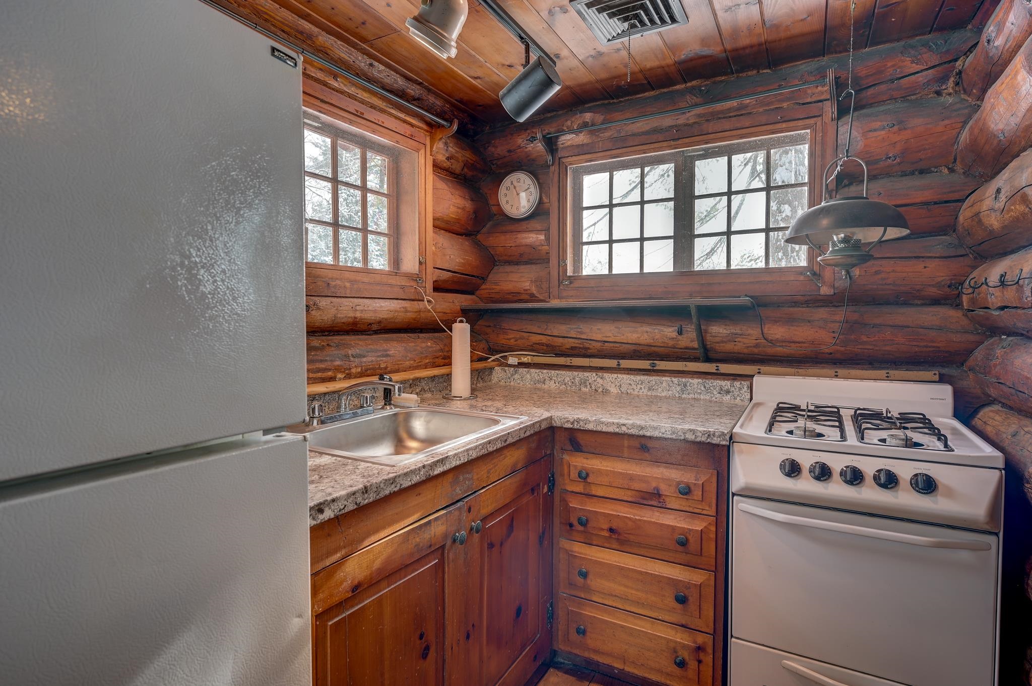 Log cabin kitchen with wood cabinets, a white gas range, and snowy trees visible through the windows.
