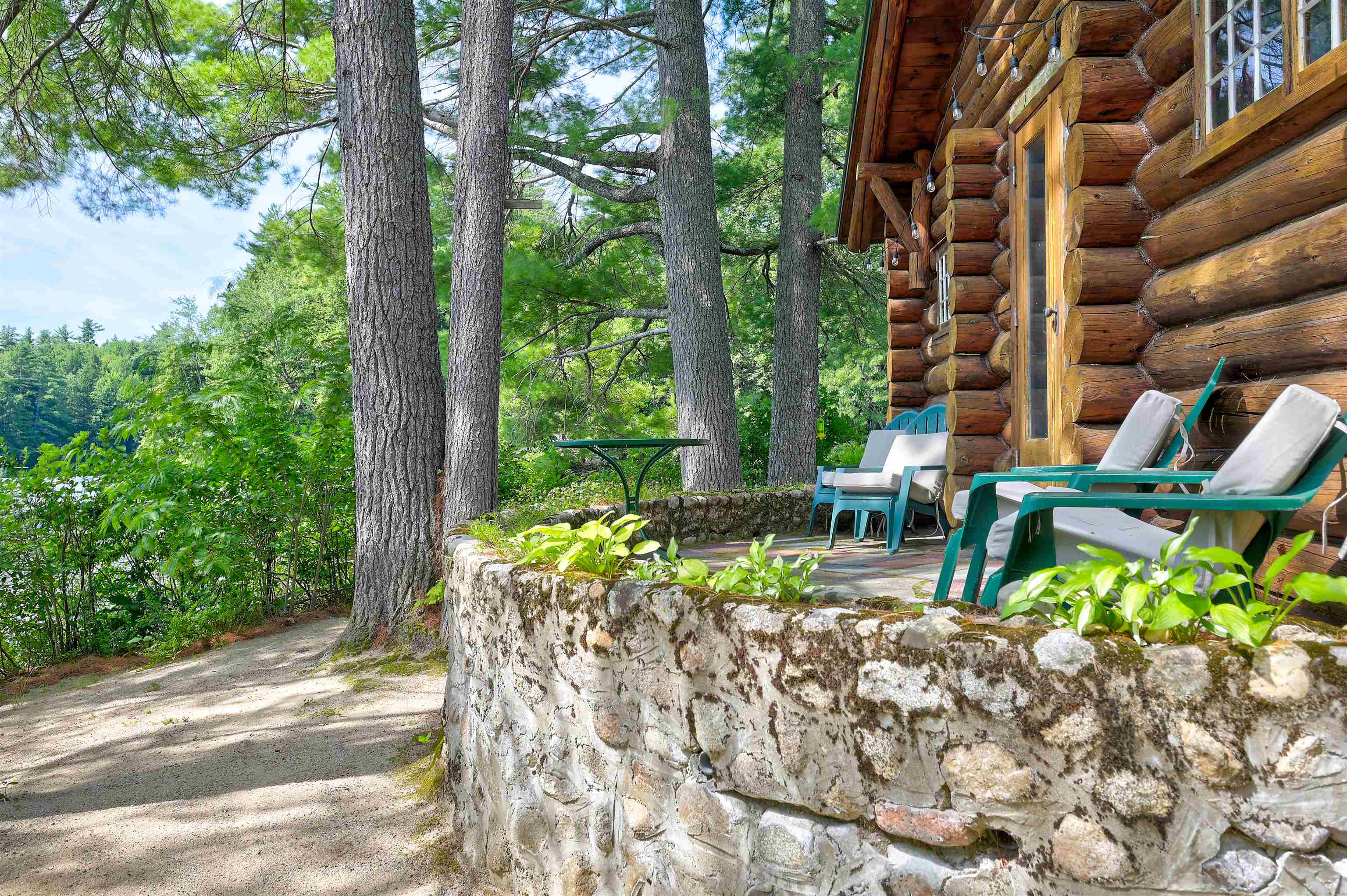 Log cabin patio with teal chairs beside a stone retaining wall in a wooded setting.