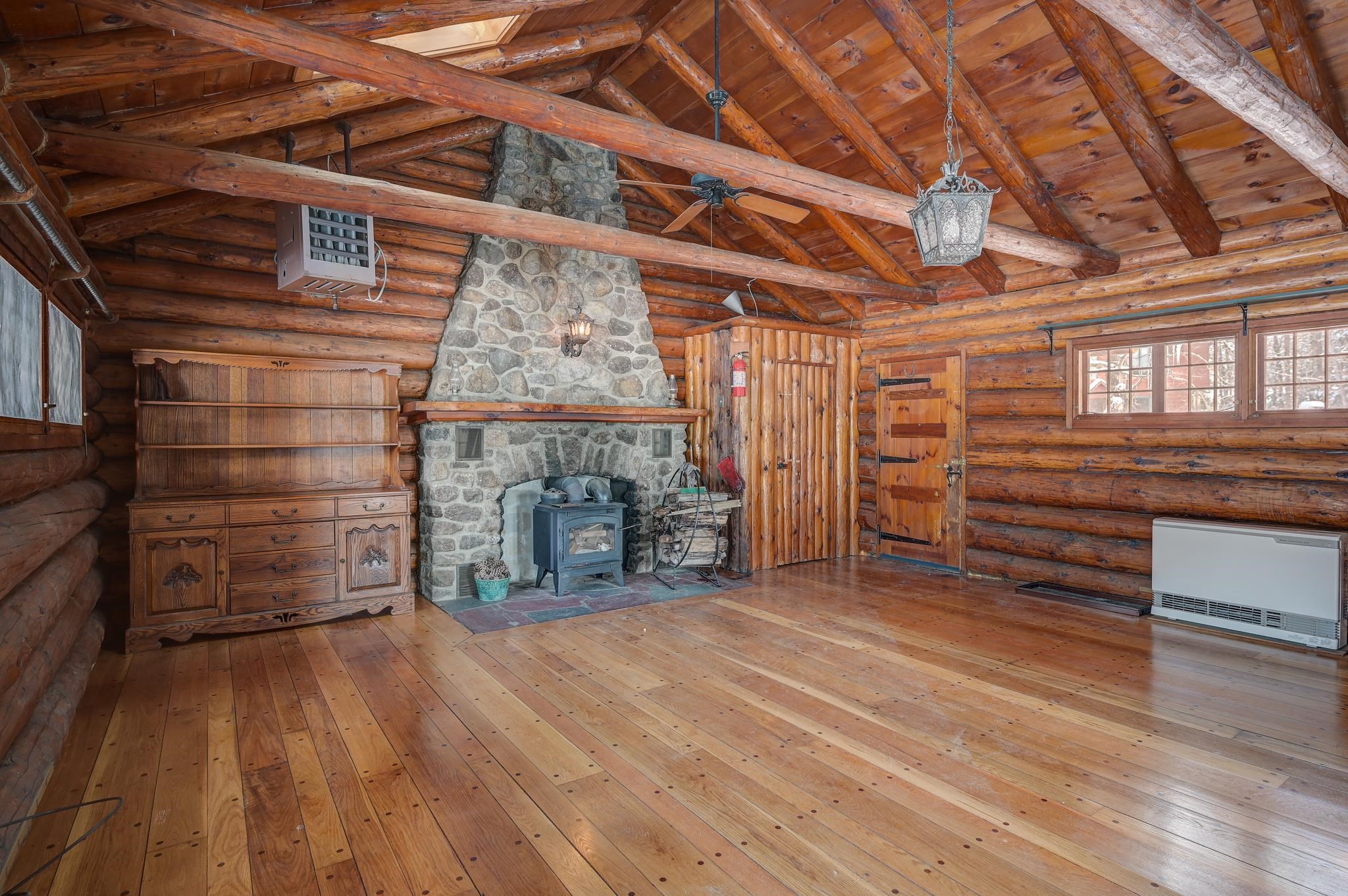 Log home living room with a stone fireplace, wood stove, and exposed timber beams.