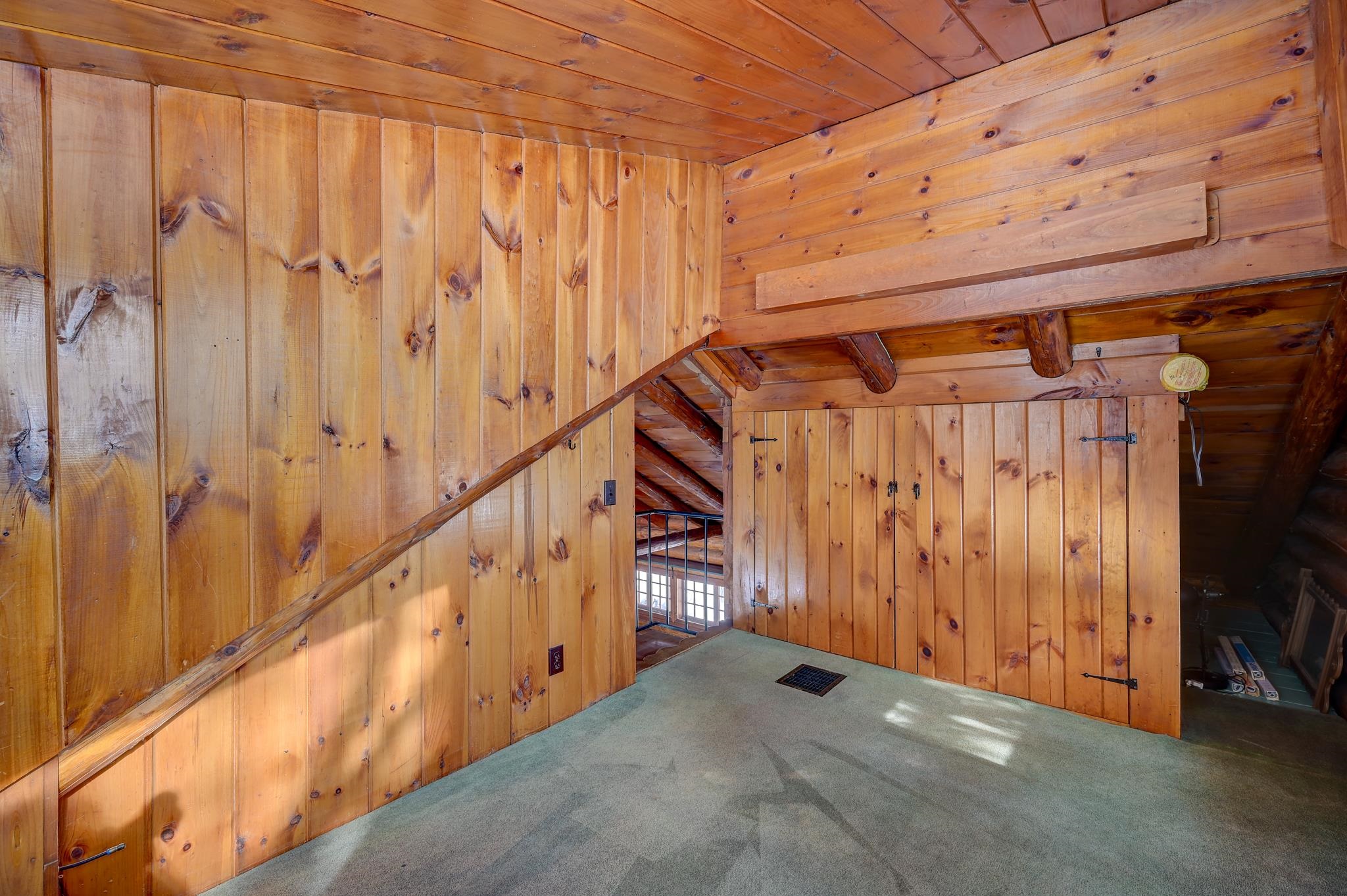 Wood-paneled interior with exposed beams, carpet, and a staircase beyond an opening.