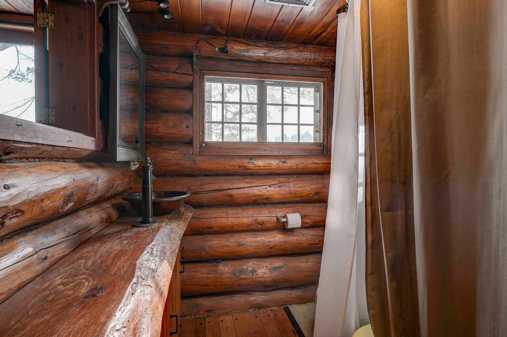 Rustic log-cabin bathroom with a vessel sink, exposed log walls, and a multi-pane window.
