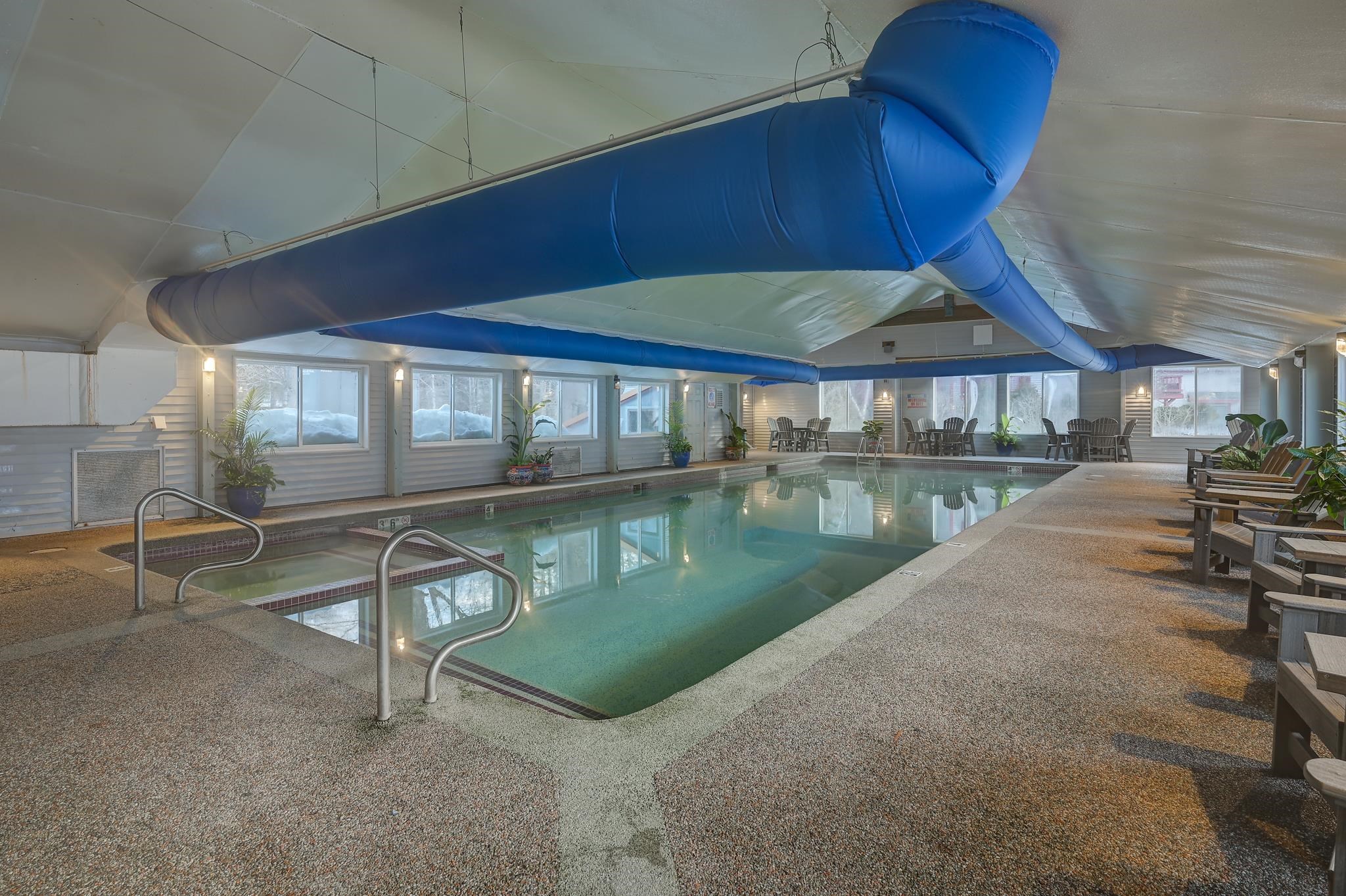 Indoor pool with a large blue overhead water slide and seating around the deck.