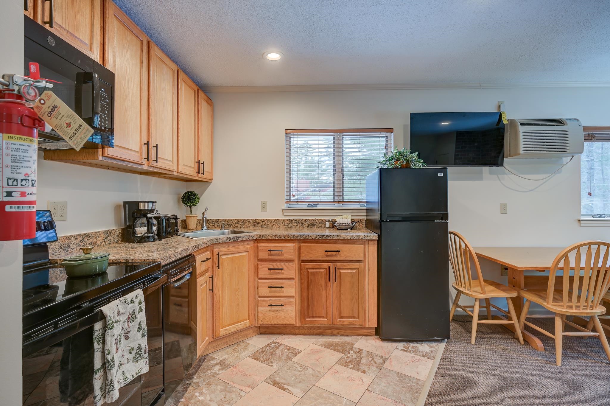 Kitchen with wood cabinets, granite counters, black appliances, and a small dining table by the windows.