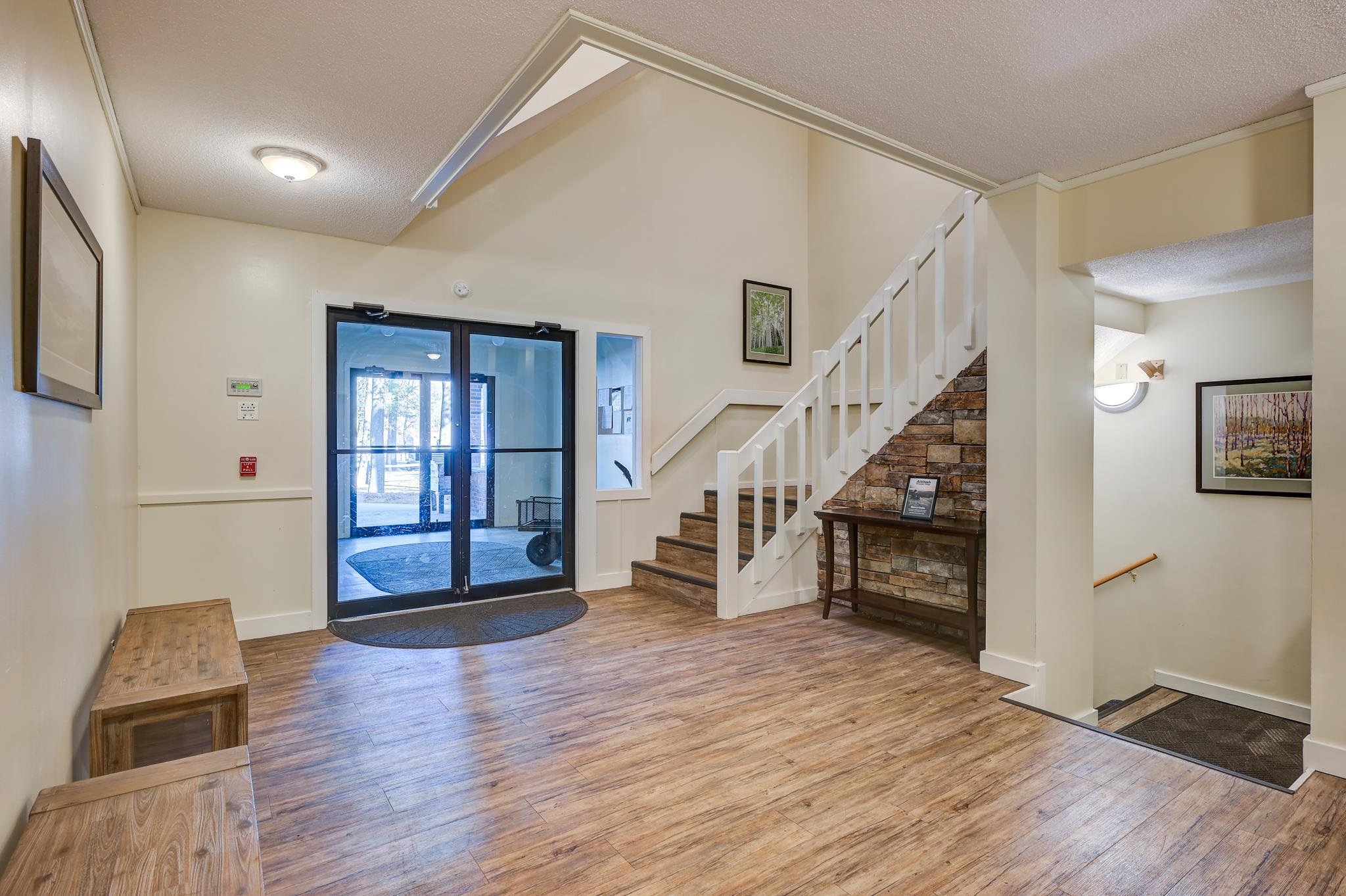 Entry foyer with glass doors, wood-look floors, and a staircase beside a stone feature wall.