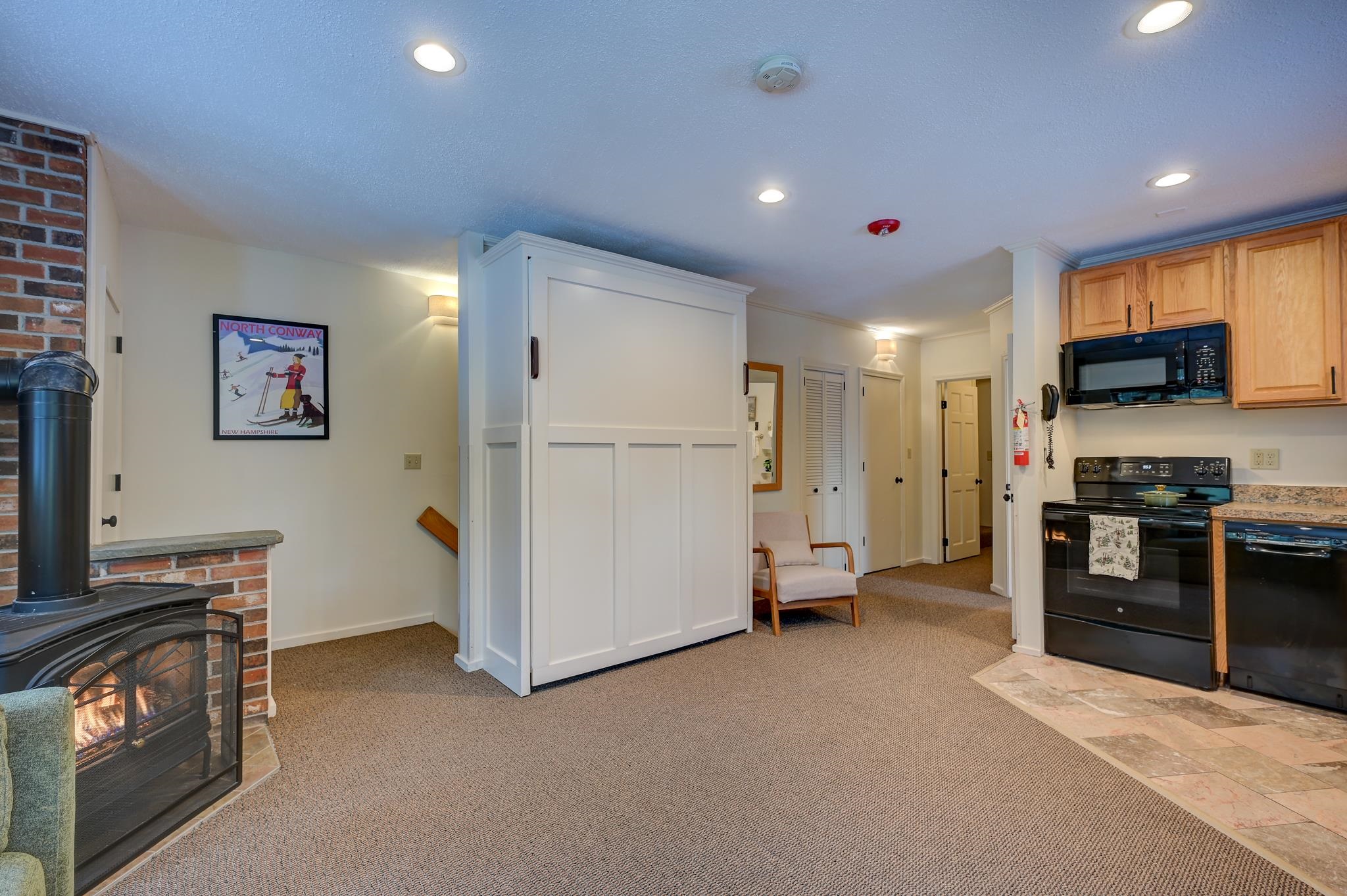 Open-plan condo living area with a brick fireplace, Murphy bed cabinet, and adjoining kitchen.