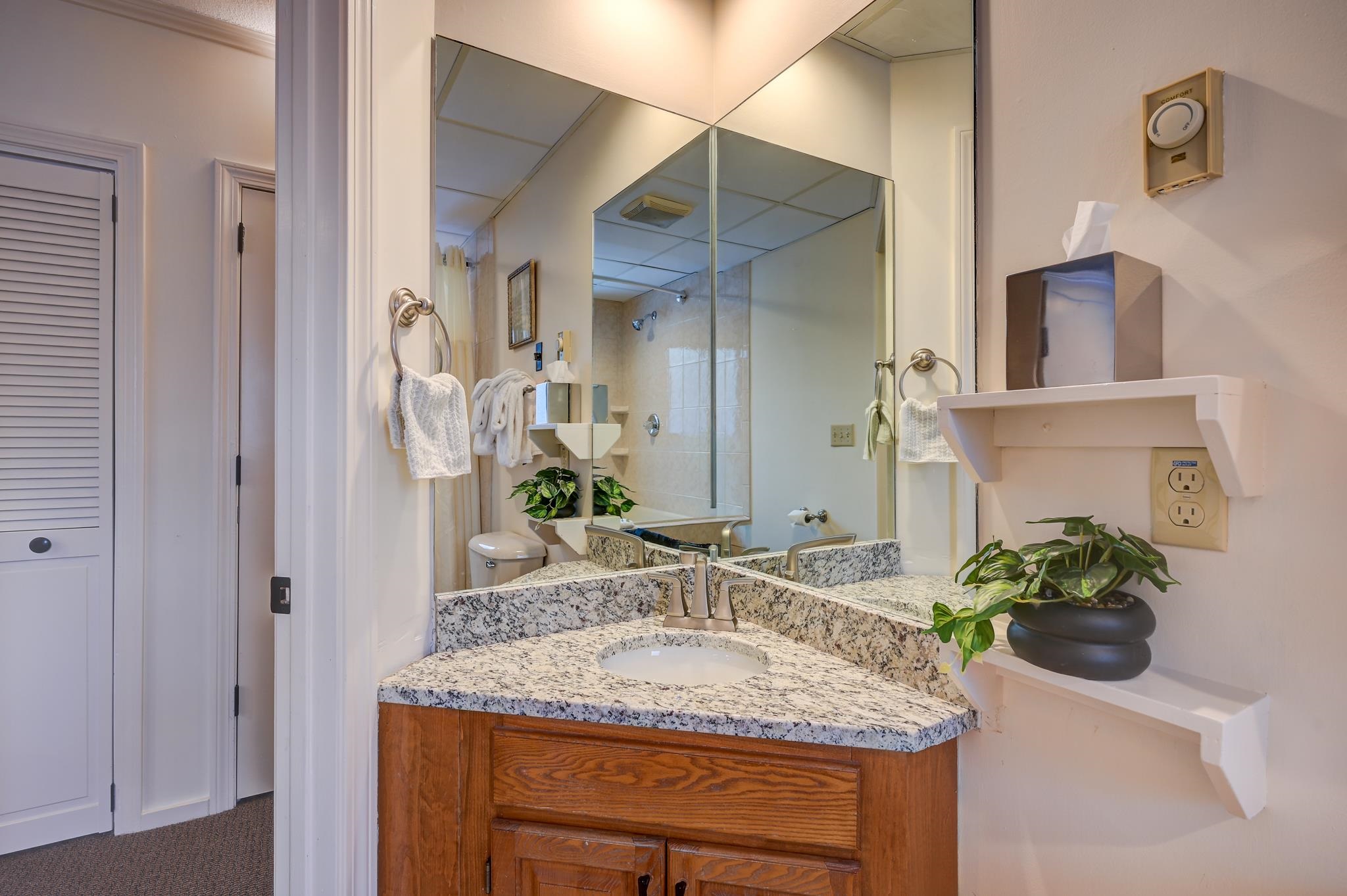 Bathroom vanity with a granite counter and large mirror reflecting a glass-enclosed shower.