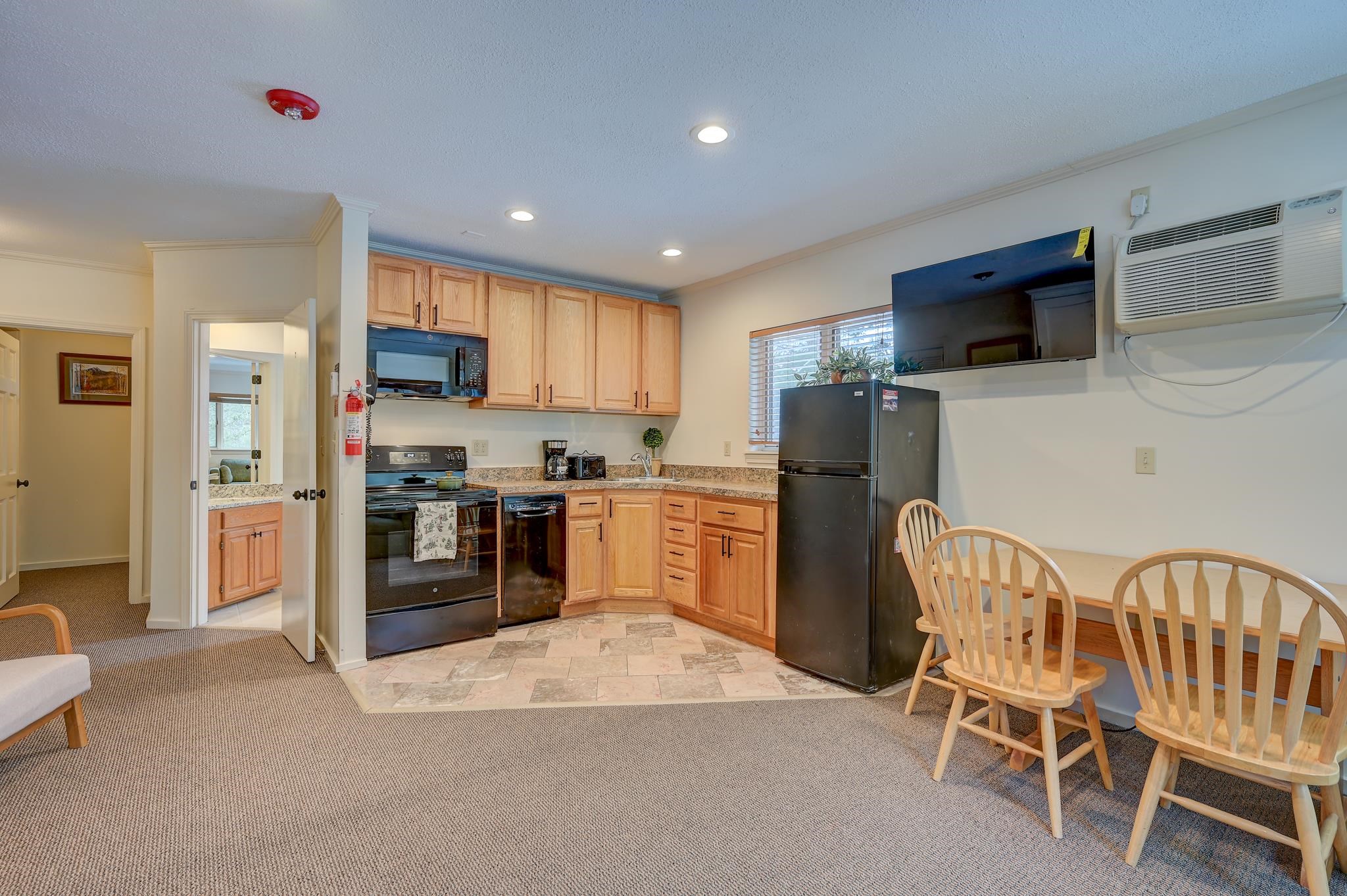 Kitchen and dining area with light wood cabinets, black appliances, and a table with wooden chairs.