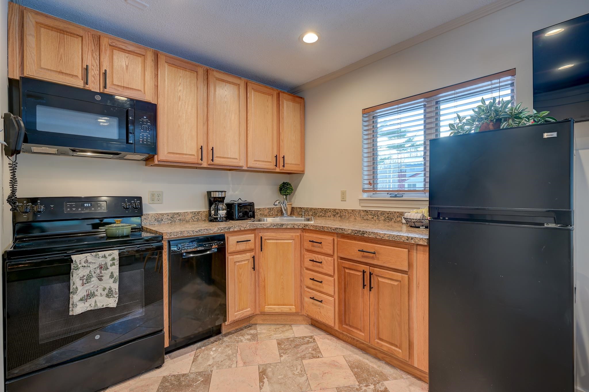 Kitchen with honey-colored wood cabinets, granite counters, black appliances, and a window above the sink.