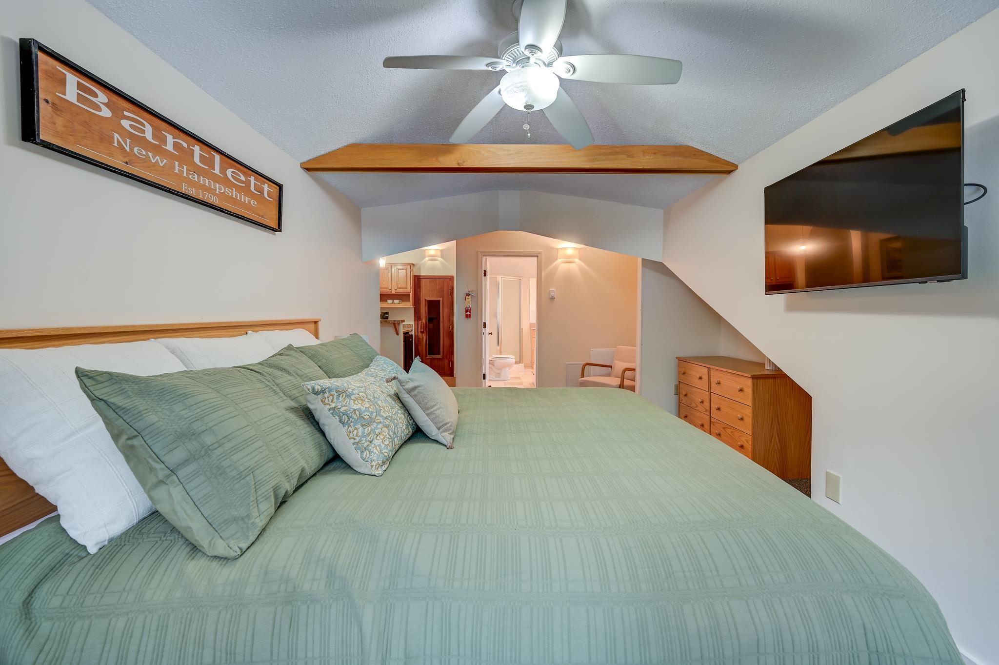 Furnished bedroom with a large green bed, wood dresser, and wall-mounted television.