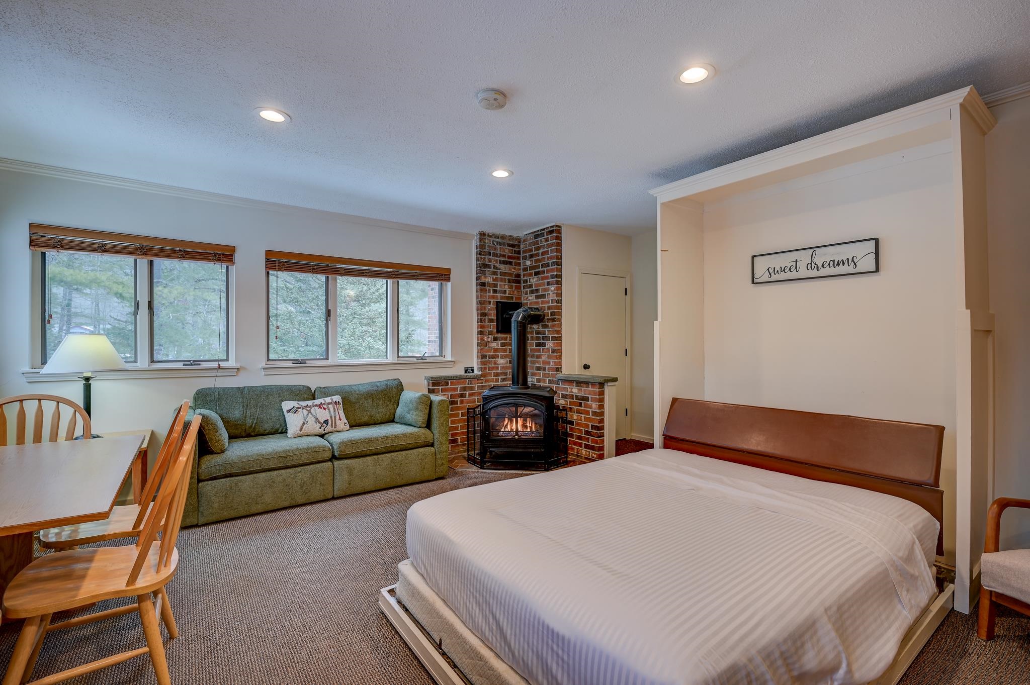 Bedroom with a large bed, green sofa, and brick-enclosed wood stove.