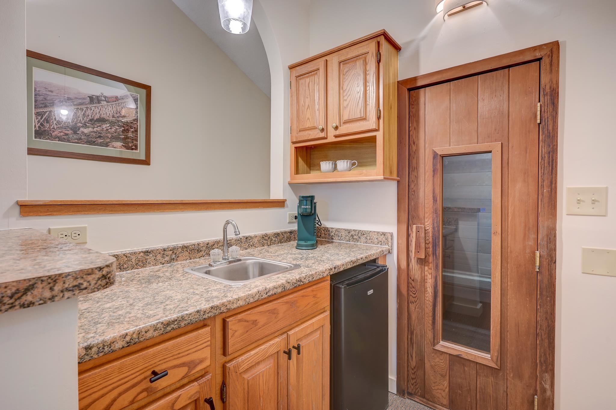 Compact kitchenette with oak cabinets, granite counters, and a wooden glass-panel sauna door.