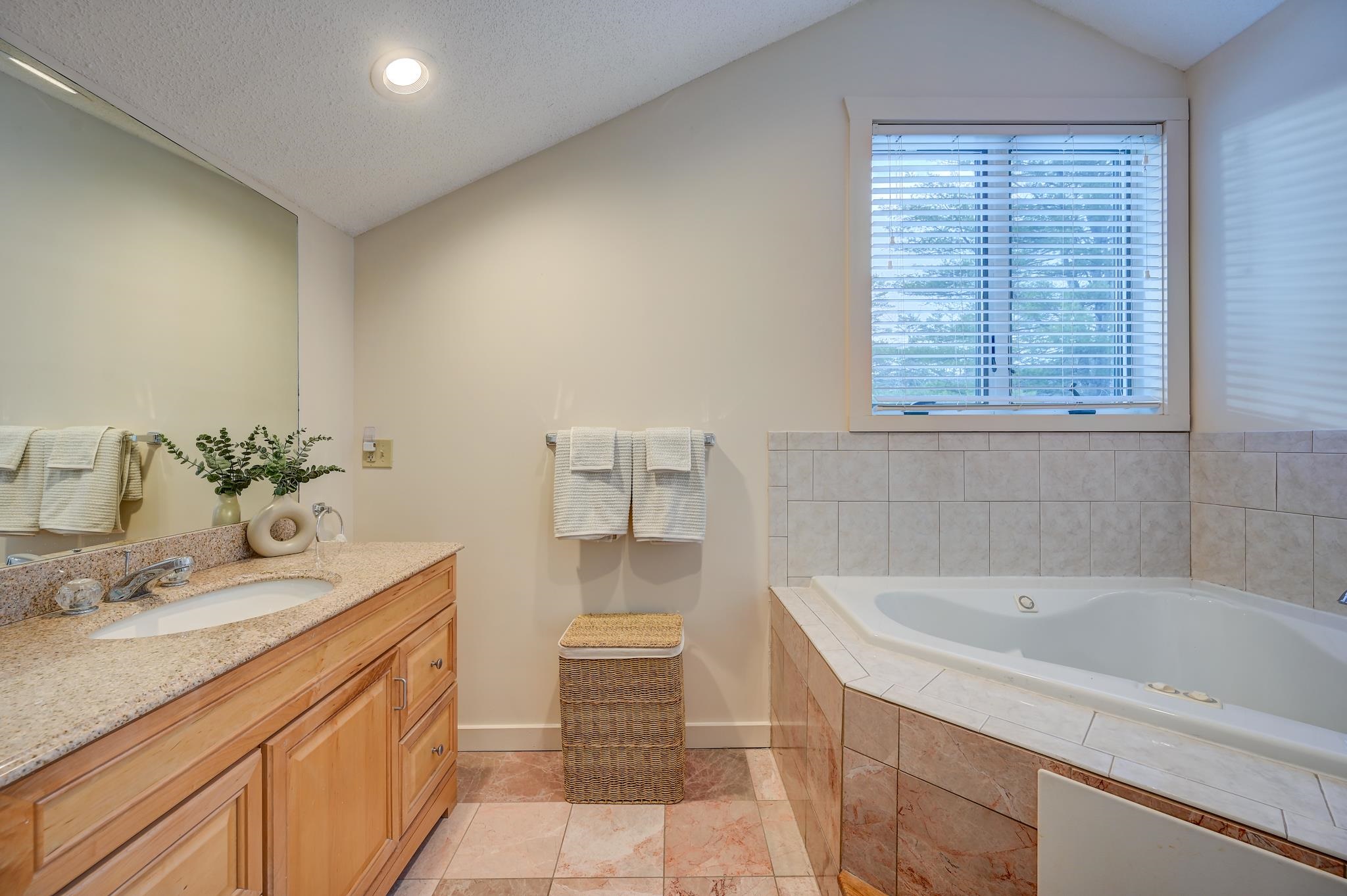 Bathroom with a built-in soaking tub beneath a window and a wood vanity with granite countertop.
