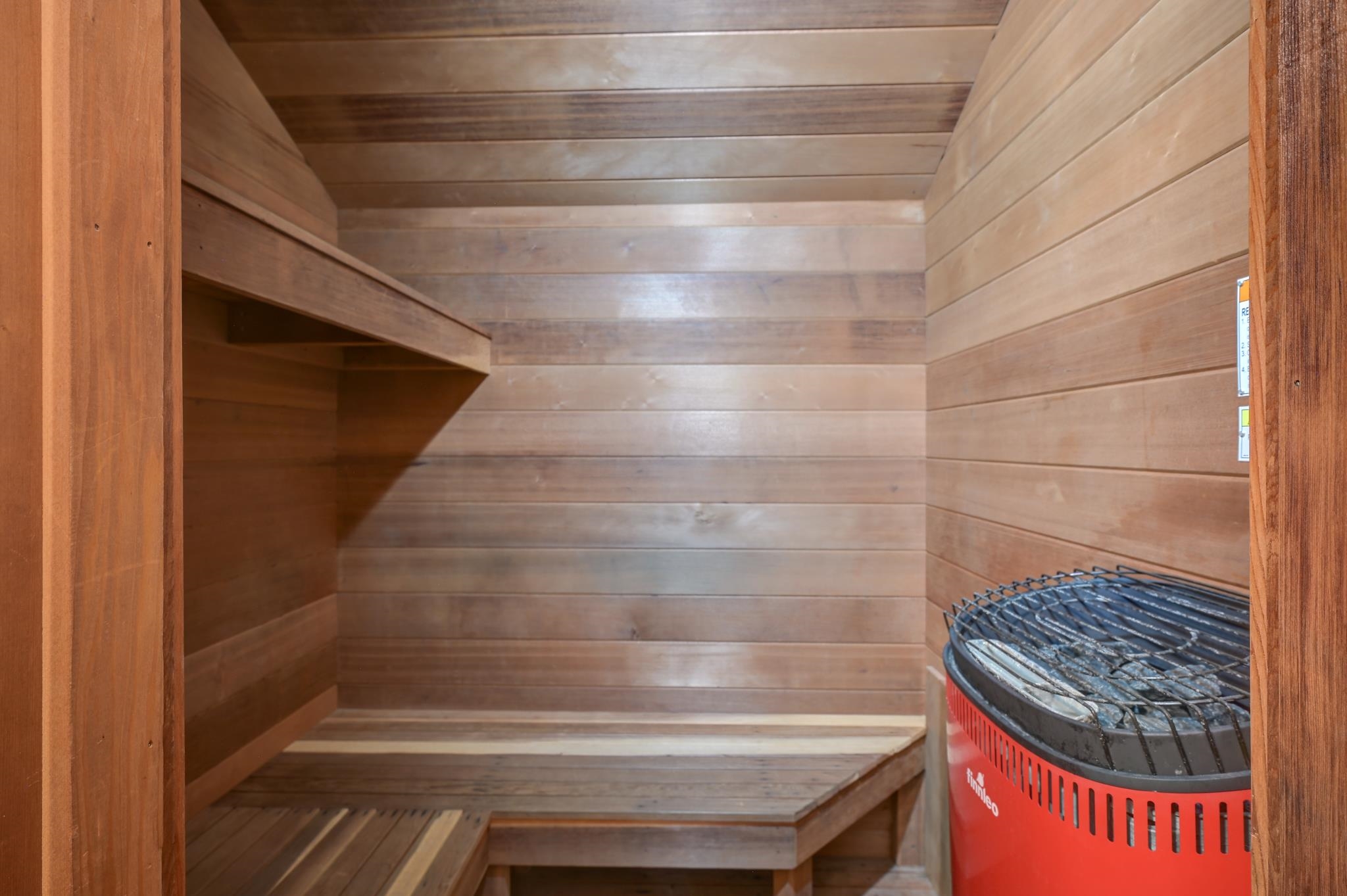 Wood-paneled sauna with tiered benches and a red electric heater.