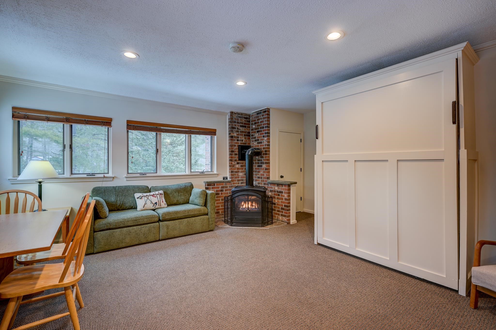 Living room with a brick-hearth wood stove, green sofa, and large white sliding door.