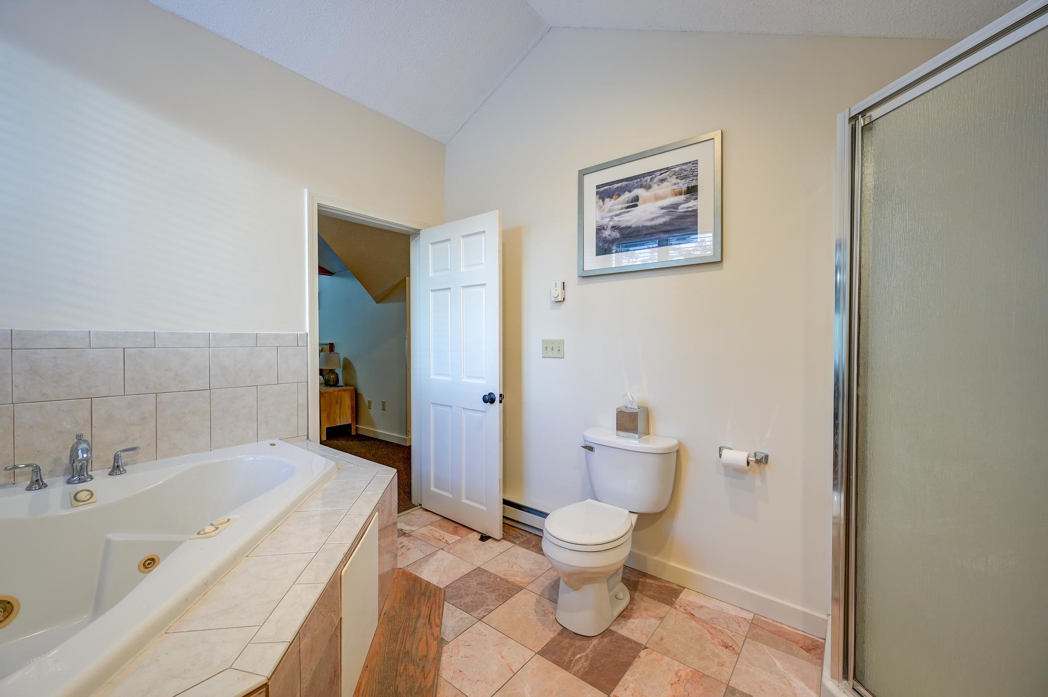 Bathroom with a corner whirlpool tub, tiled floor, toilet, and glass-enclosed shower.