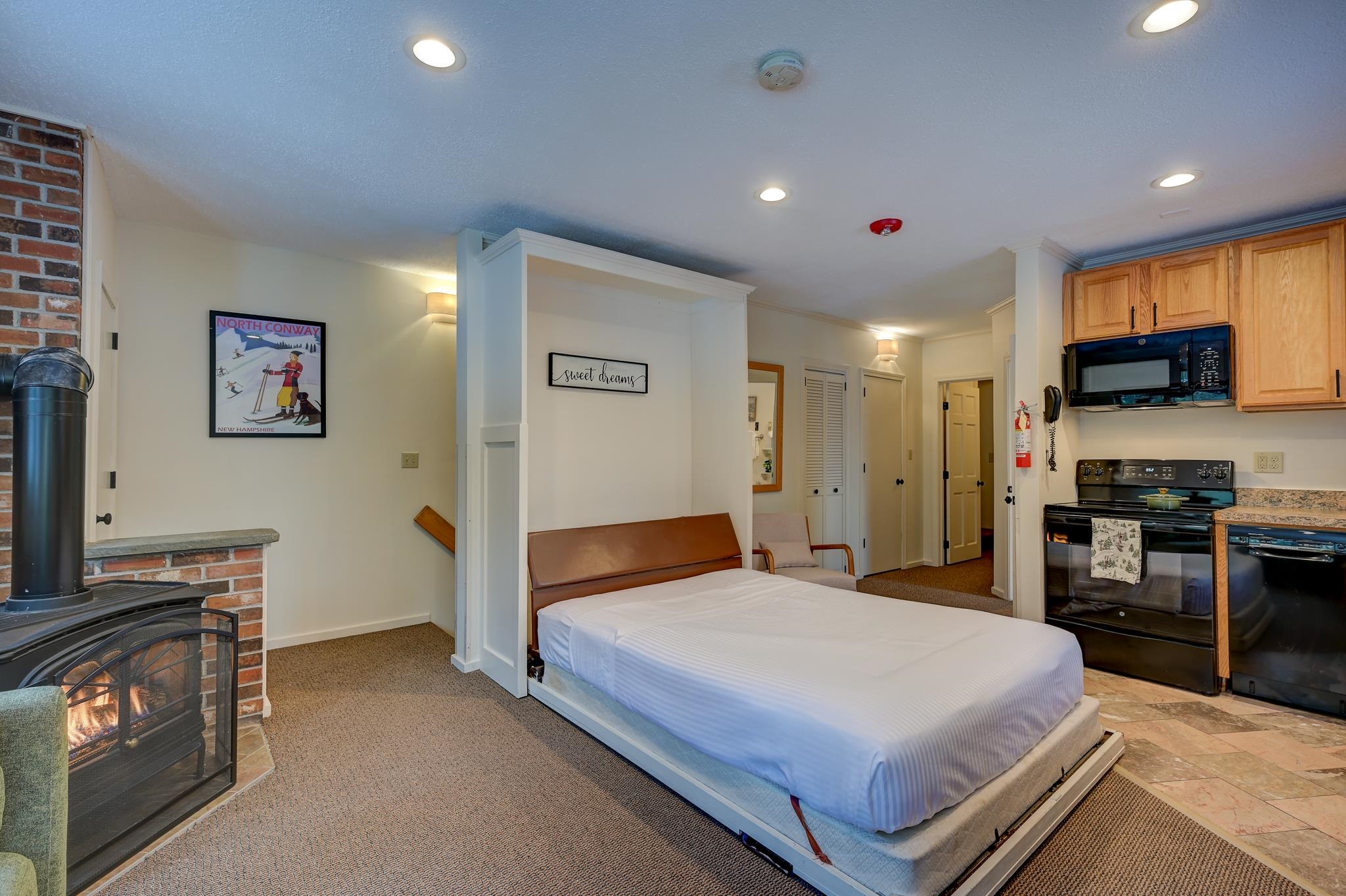 Studio room with a lowered Murphy bed, brick fireplace, and compact kitchenette.