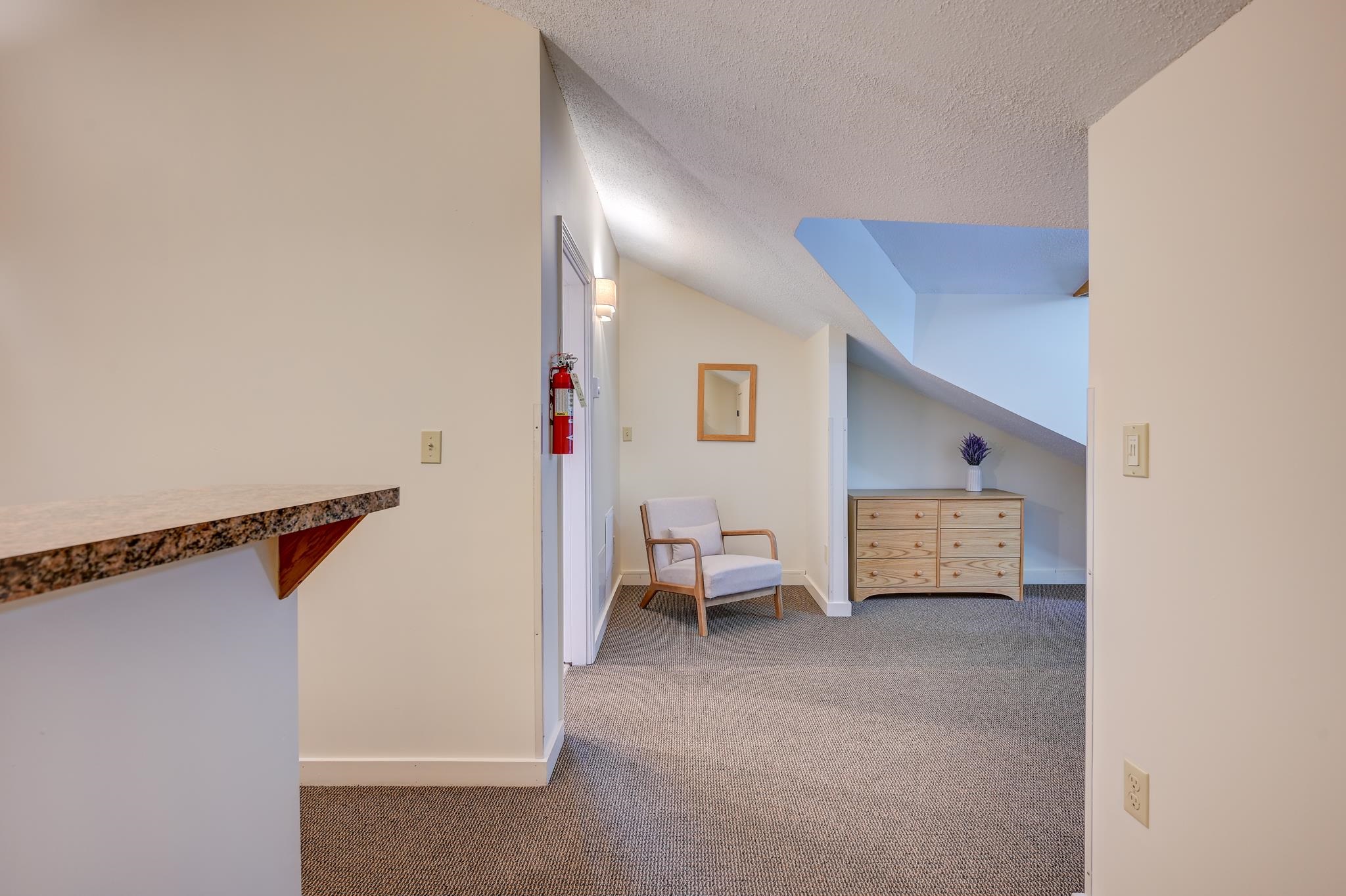 Carpeted loft landing with a skylight, wood dresser, upholstered chair, and built-in counter.