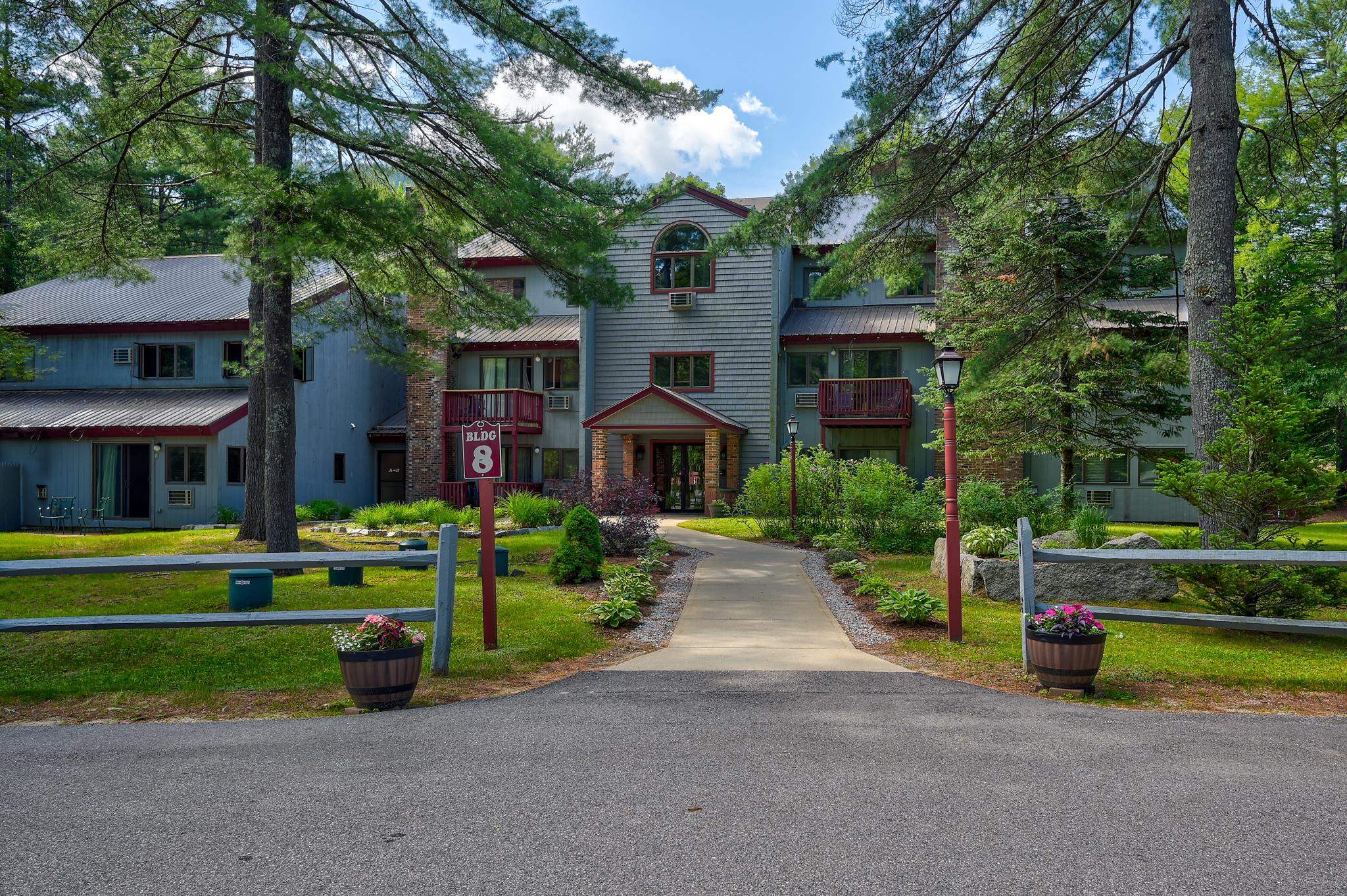 Residential building marked BLDG 8, approached by a landscaped walkway beneath mature trees.