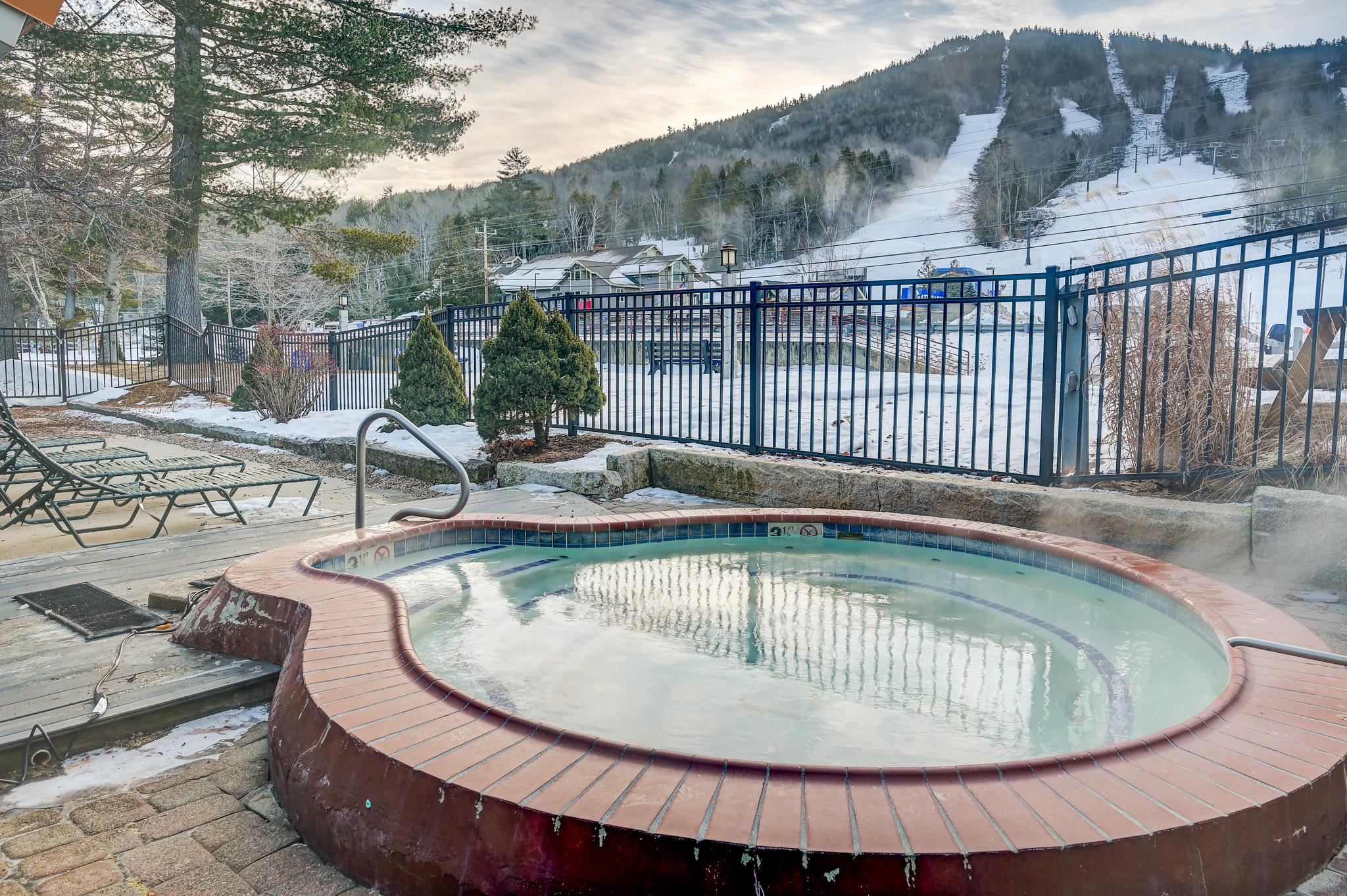 Outdoor pool and raised spa beside a snowy deck, with ski trails on the mountain beyond.