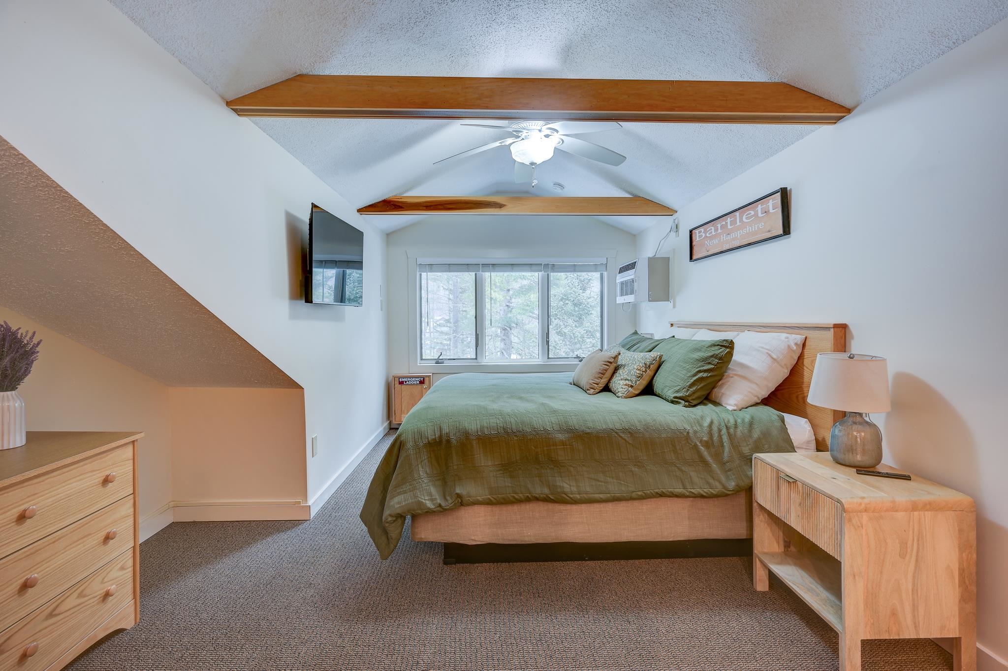 Attic bedroom with green bedding, exposed wooden beams, and a window overlooking trees.