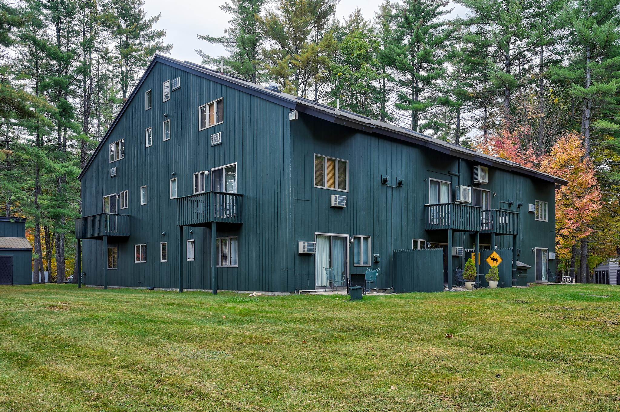 Dark teal multi-unit building with balconies and window air conditioners, surrounded by trees.