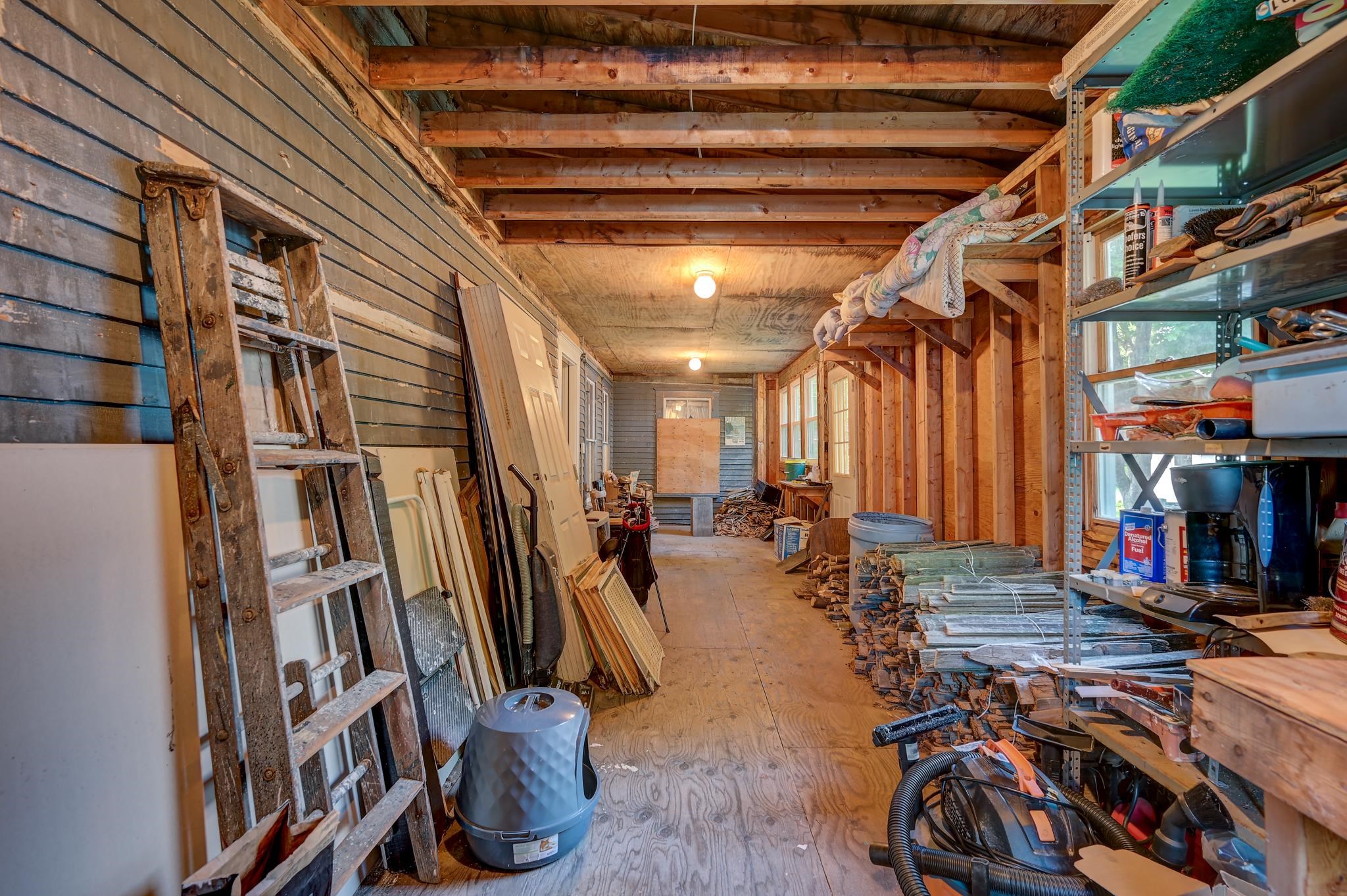 Unfinished workshop lined with ladders, tools, doors, and stacks of lumber.
