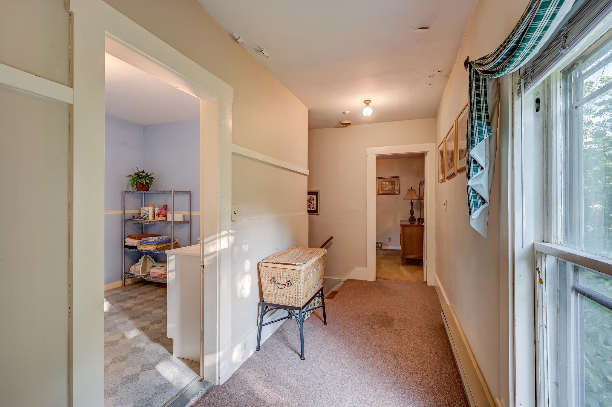 Carpeted hallway with large windows, plaid curtains, and a wicker laundry hamper beside a utility area.