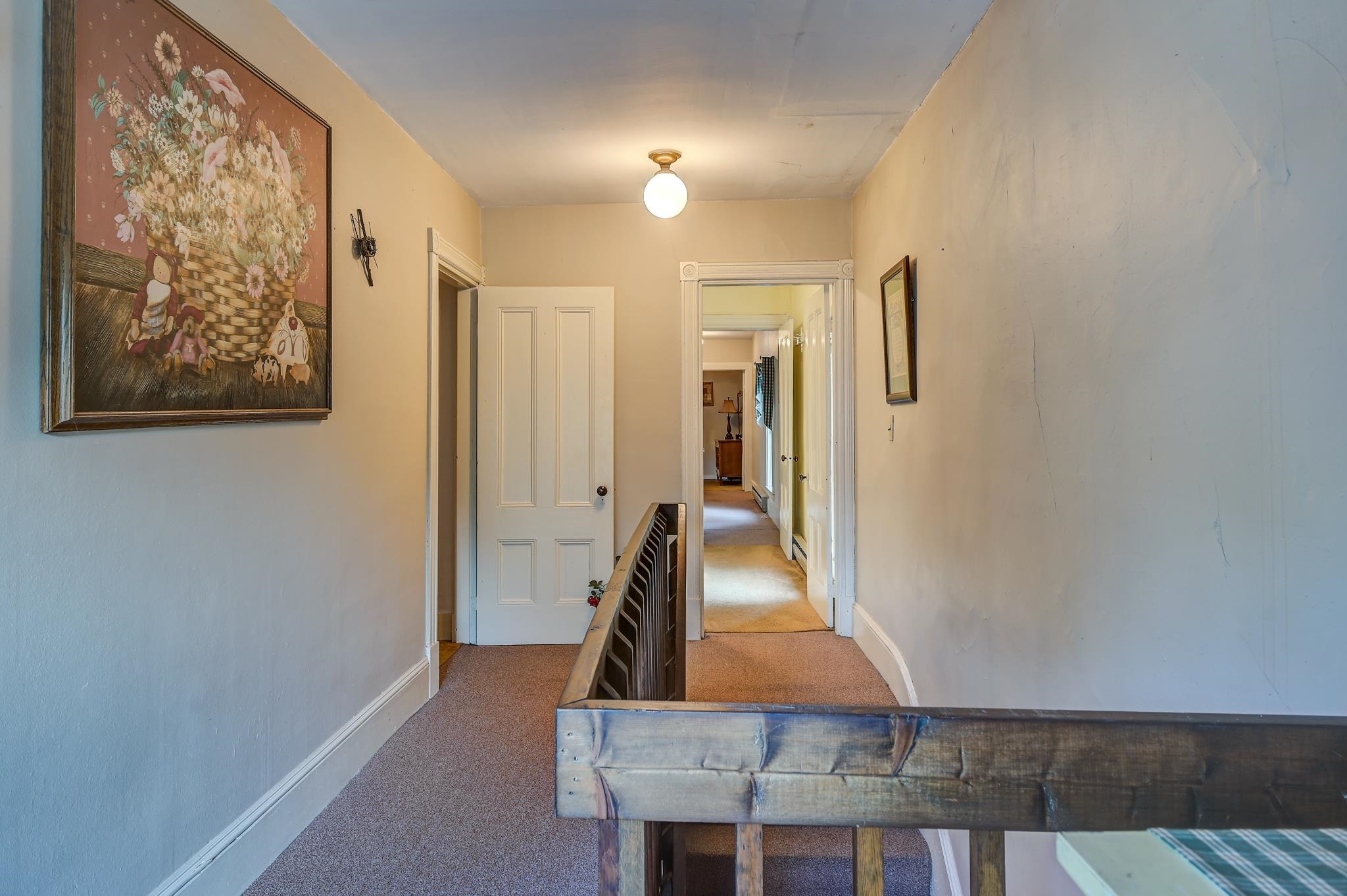 Upstairs hallway with a wooden stair railing, beige carpet, and a large floral painting.
