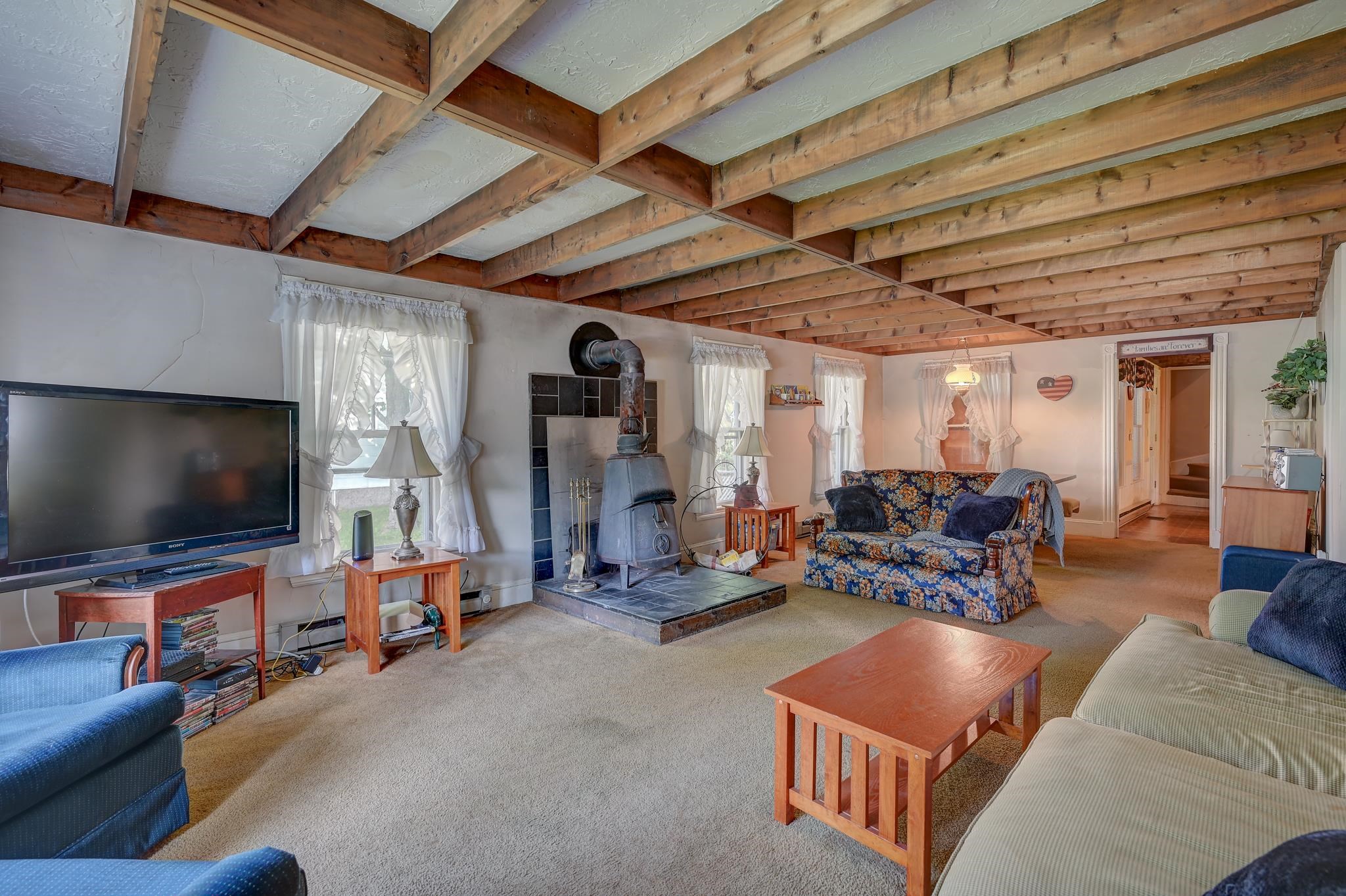 Living room with exposed timber ceiling beams and a freestanding wood stove.