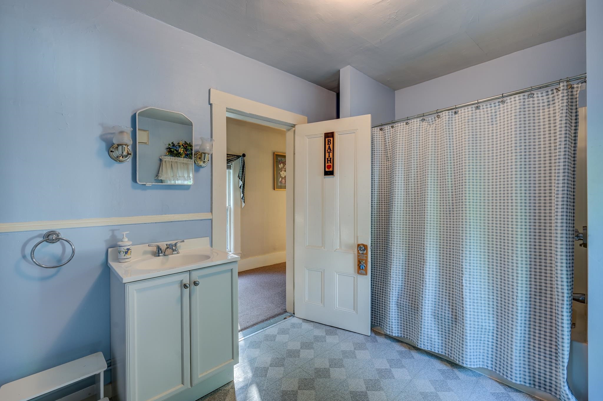 Bathroom with a pale blue vanity, mirrored wall lights, and a checked shower curtain.
