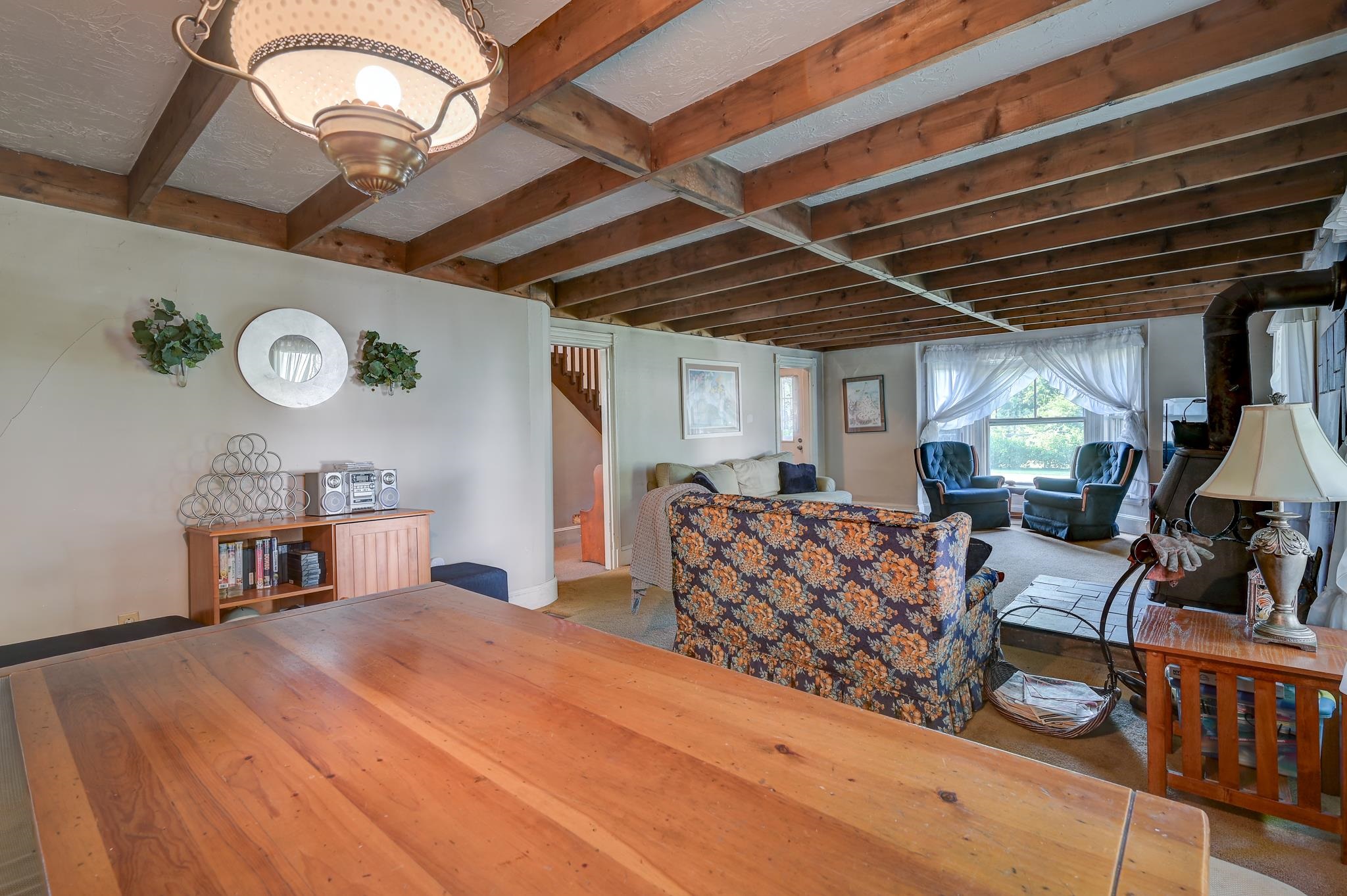 Living room with exposed wooden beams, floral sofa, blue armchairs, and a wood stove.