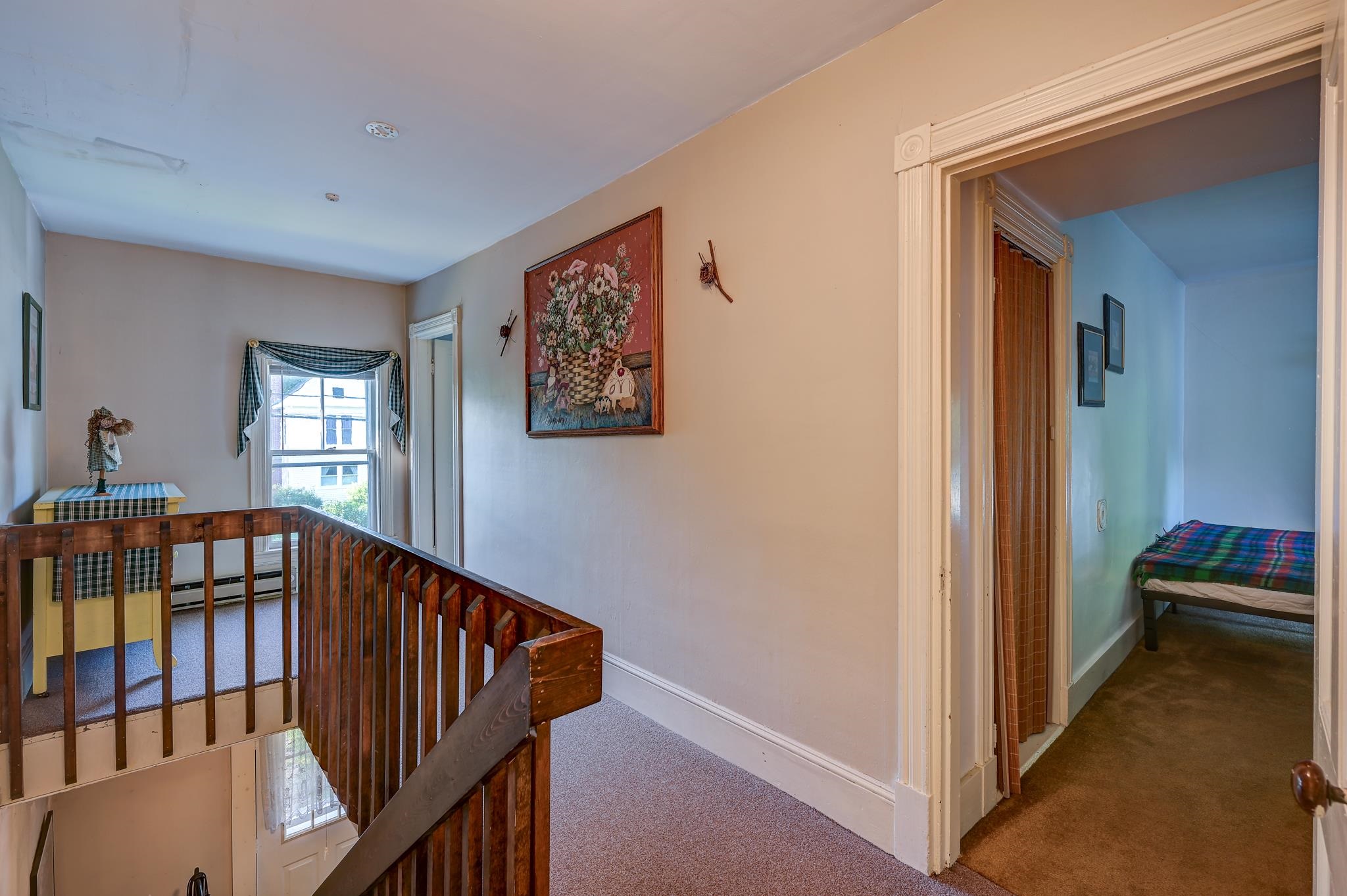 Upstairs landing with a wooden stair railing and a bedroom through the doorway.