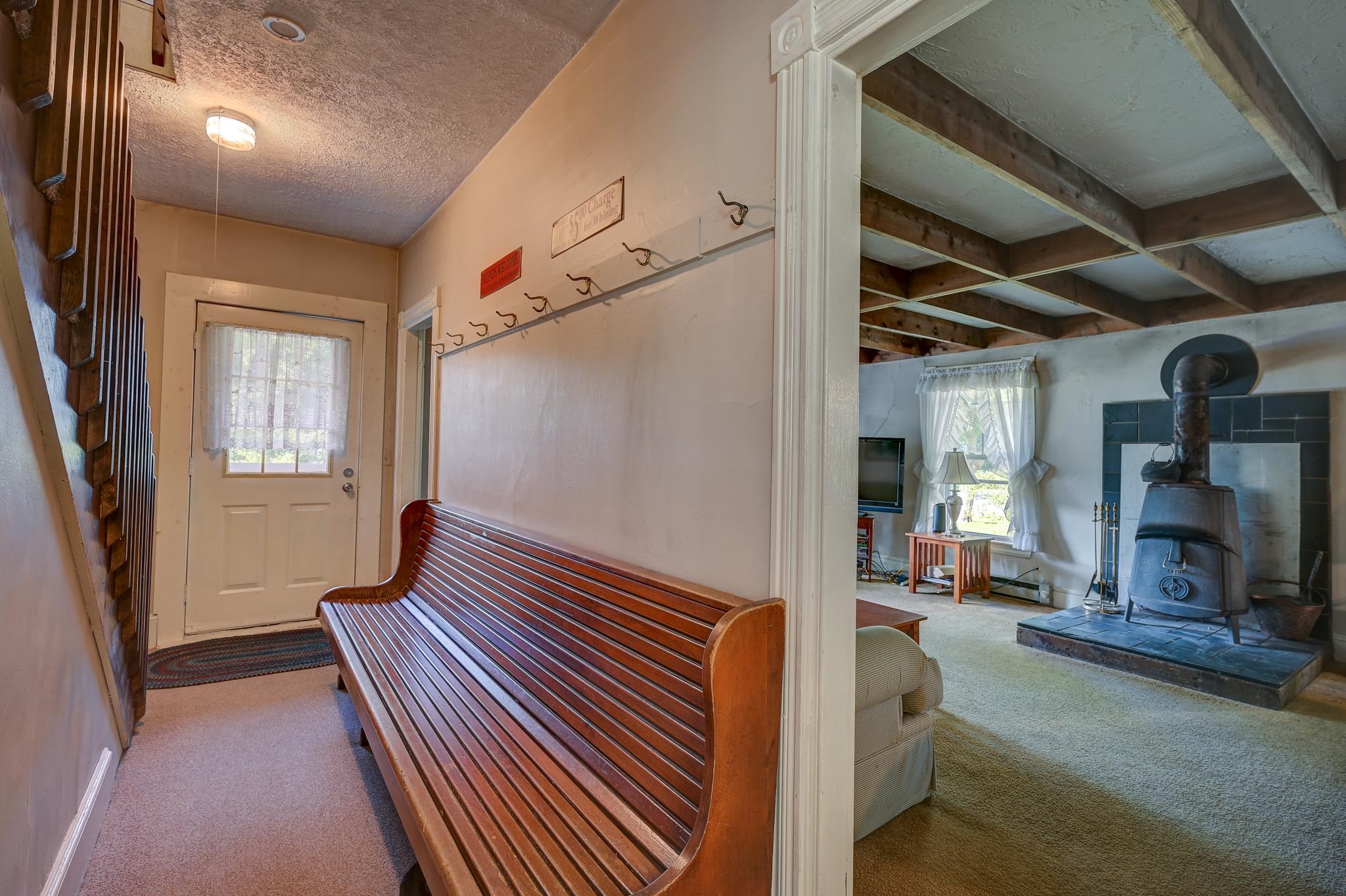 Entry hallway with a long wooden bench opens to a living room with exposed beams and a wood stove.