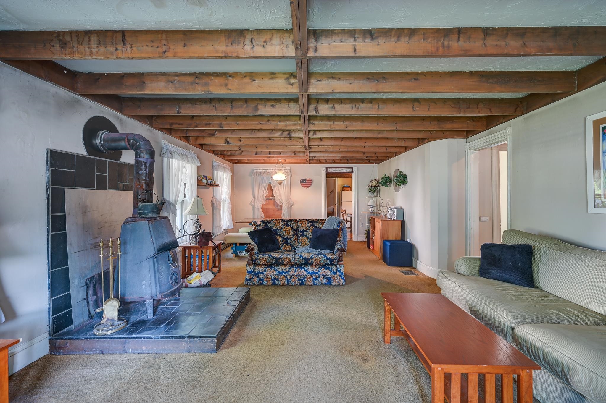Furnished living room with exposed timber beams and a freestanding wood stove.