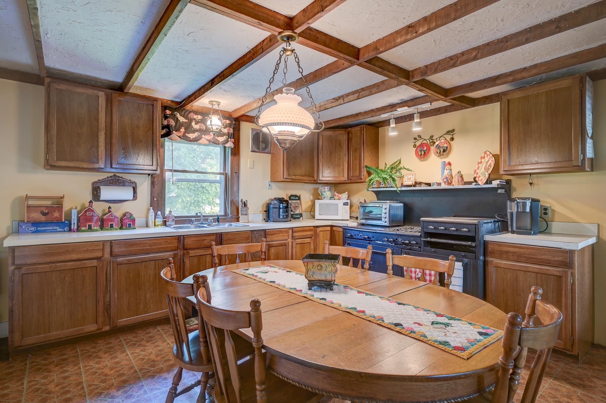 Kitchen and dining area with exposed beams, dark wood cabinets, and a large table.