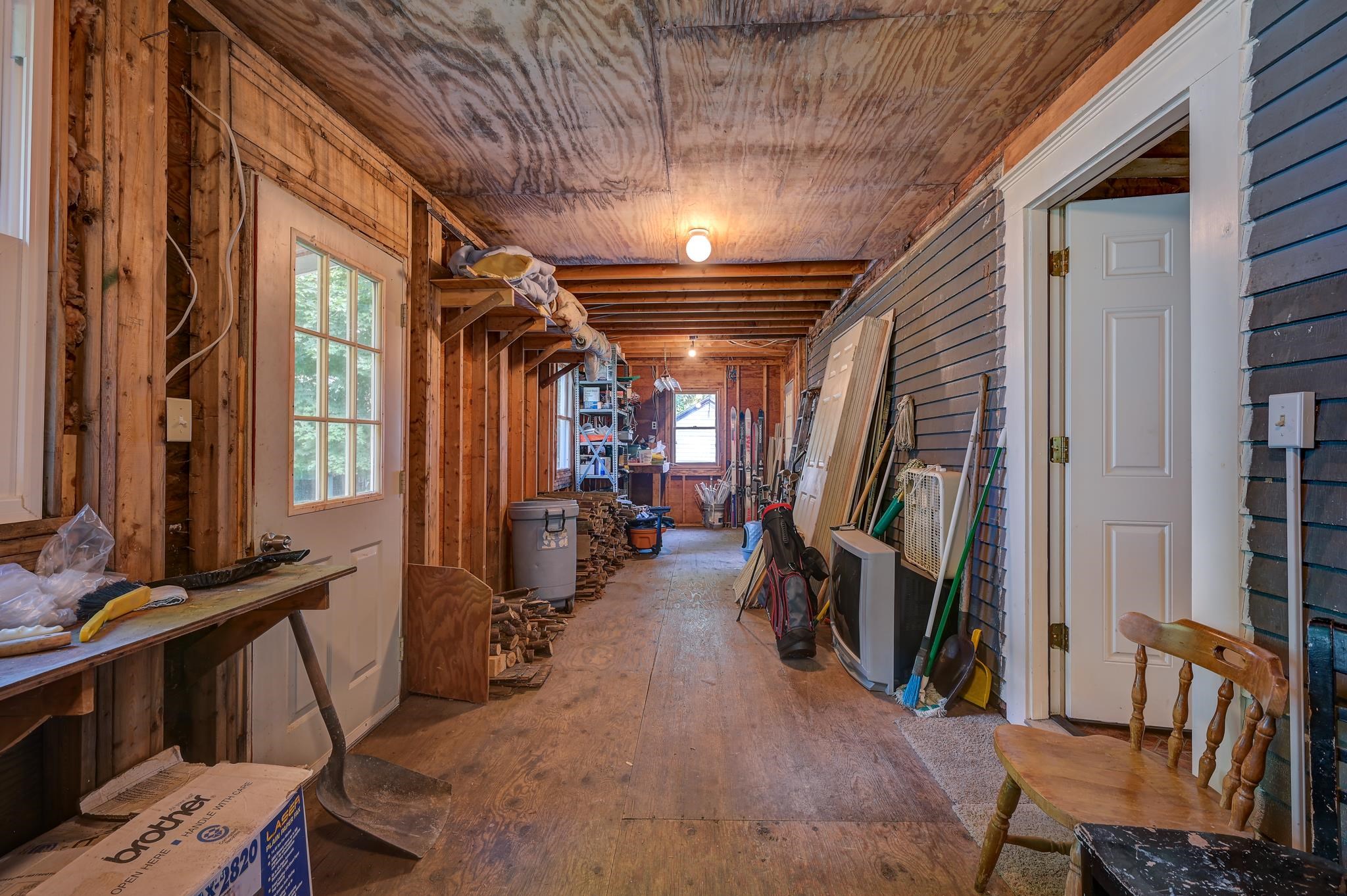 Garage workshop with exposed framing, stored tools, firewood, and a windowed door.