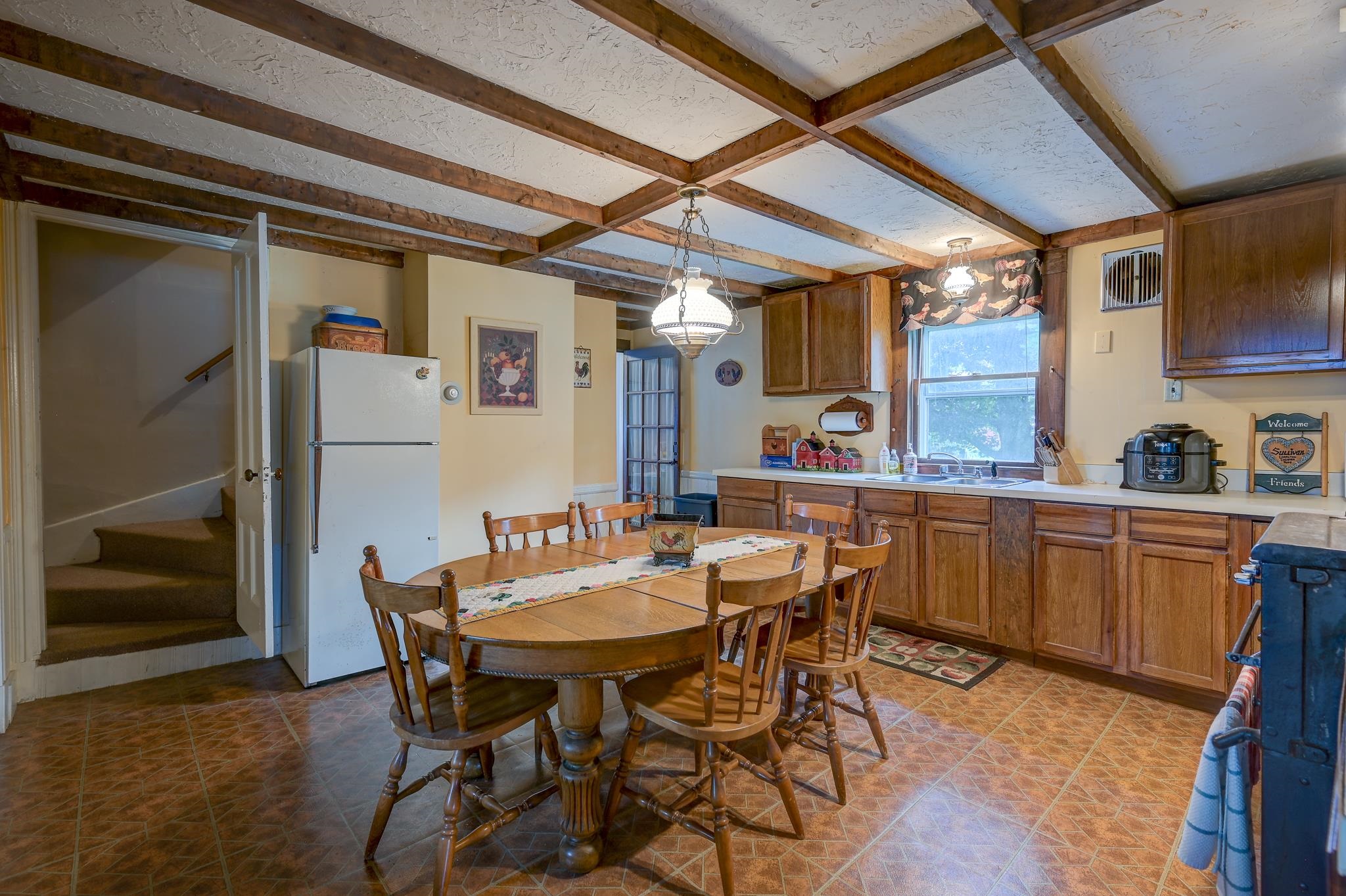 Kitchen and dining area with exposed ceiling beams, wooden cabinetry, and an oval table.