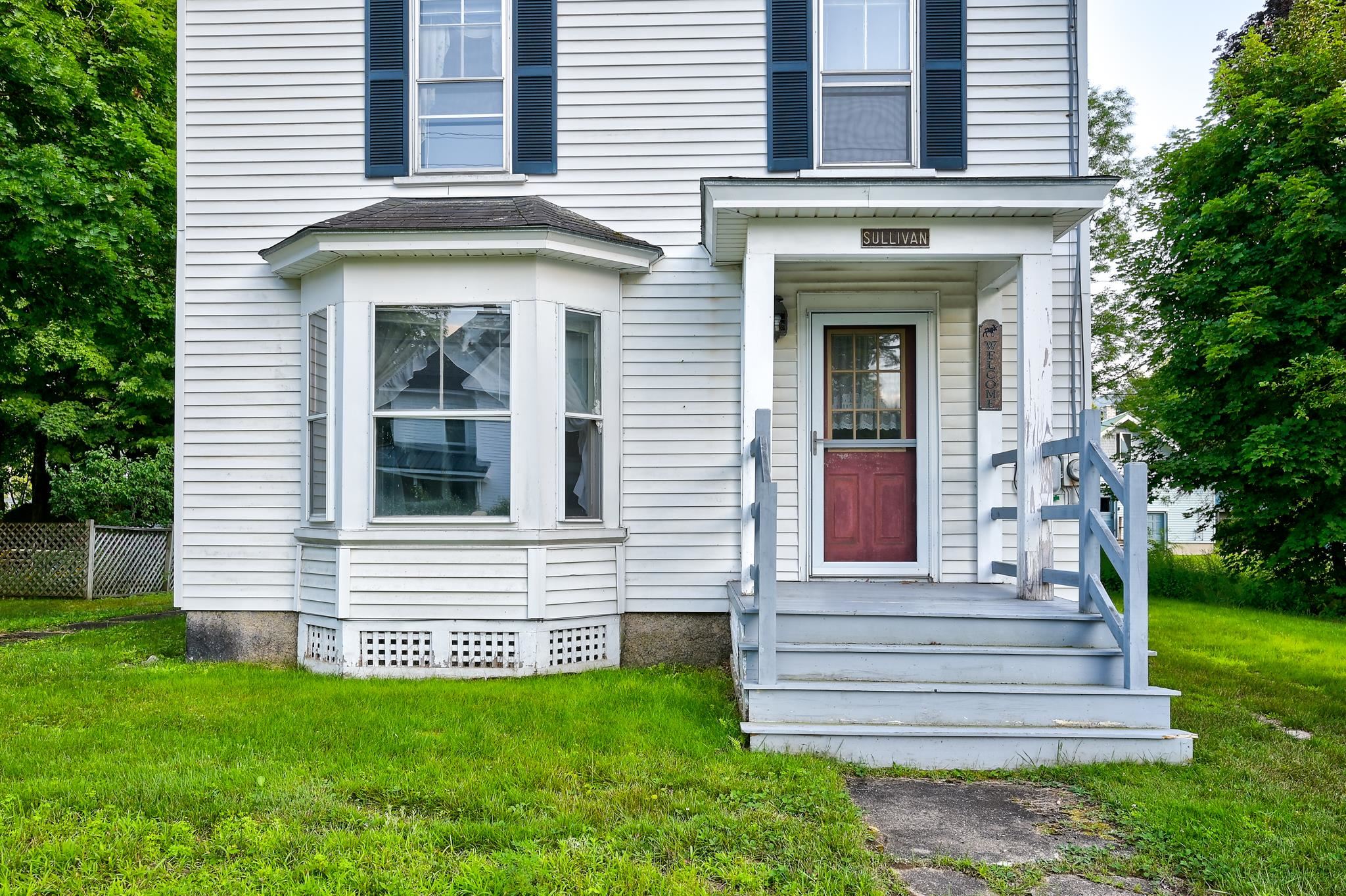 White two-story house with a bay window, covered porch, blue-gray railings, and red front door.